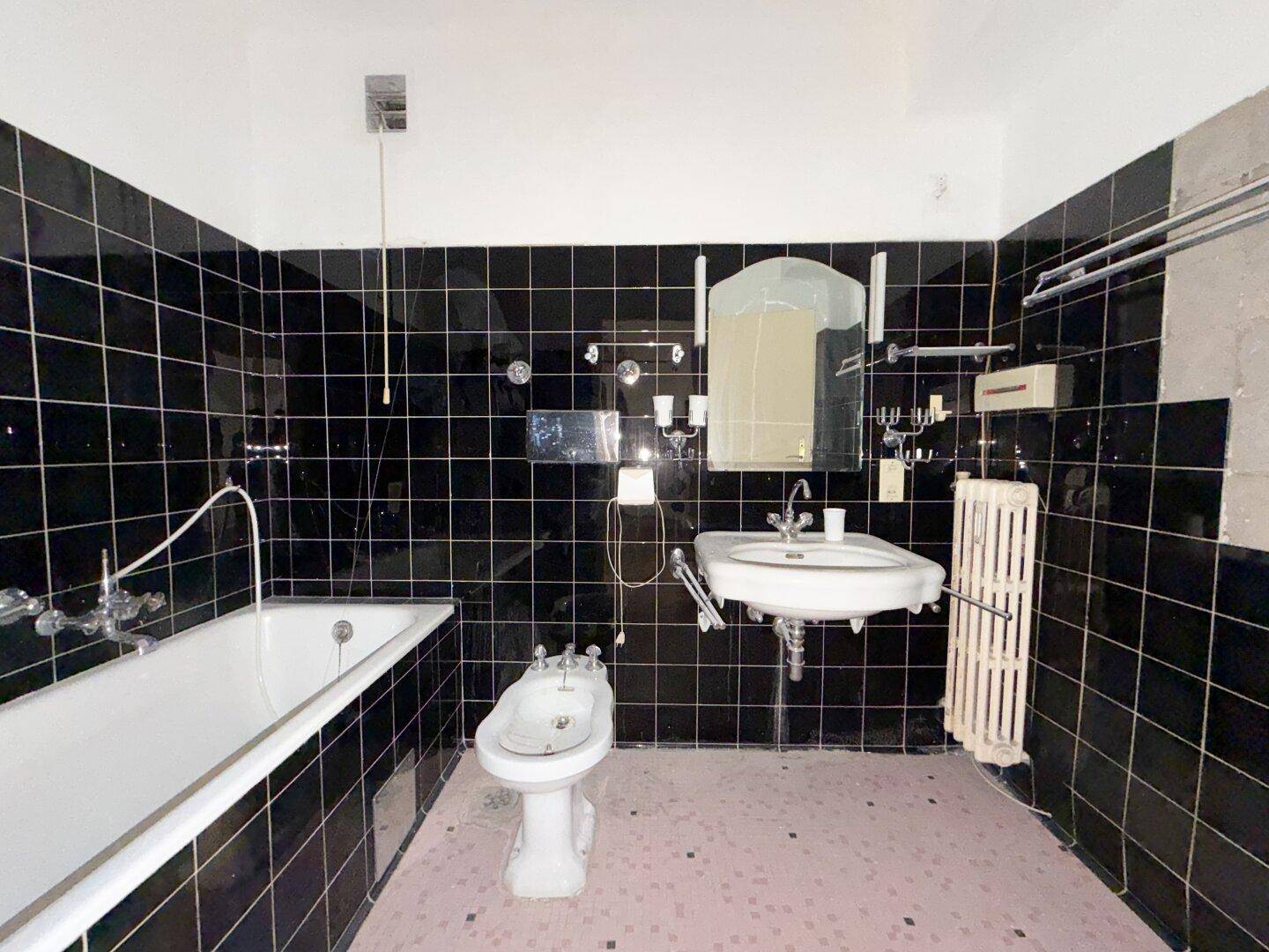 Badezimmer mit schwarzen Fliesen, Badewanne, Bidet und einem einzelnen Waschbecken.