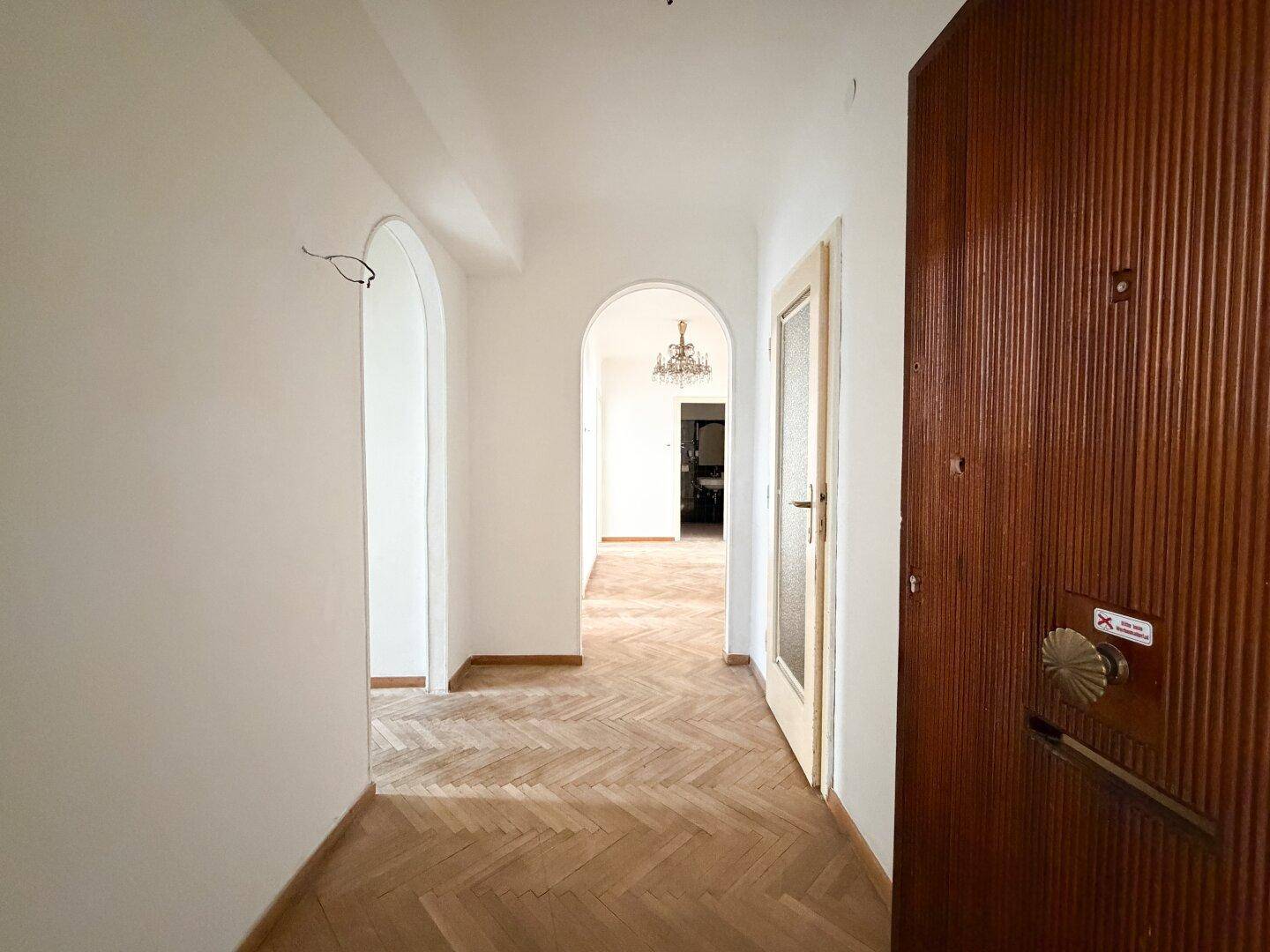 Heller Eingangsbereich mit Fischgrätparkett, Holztür und einem eleganten Rundbogen.