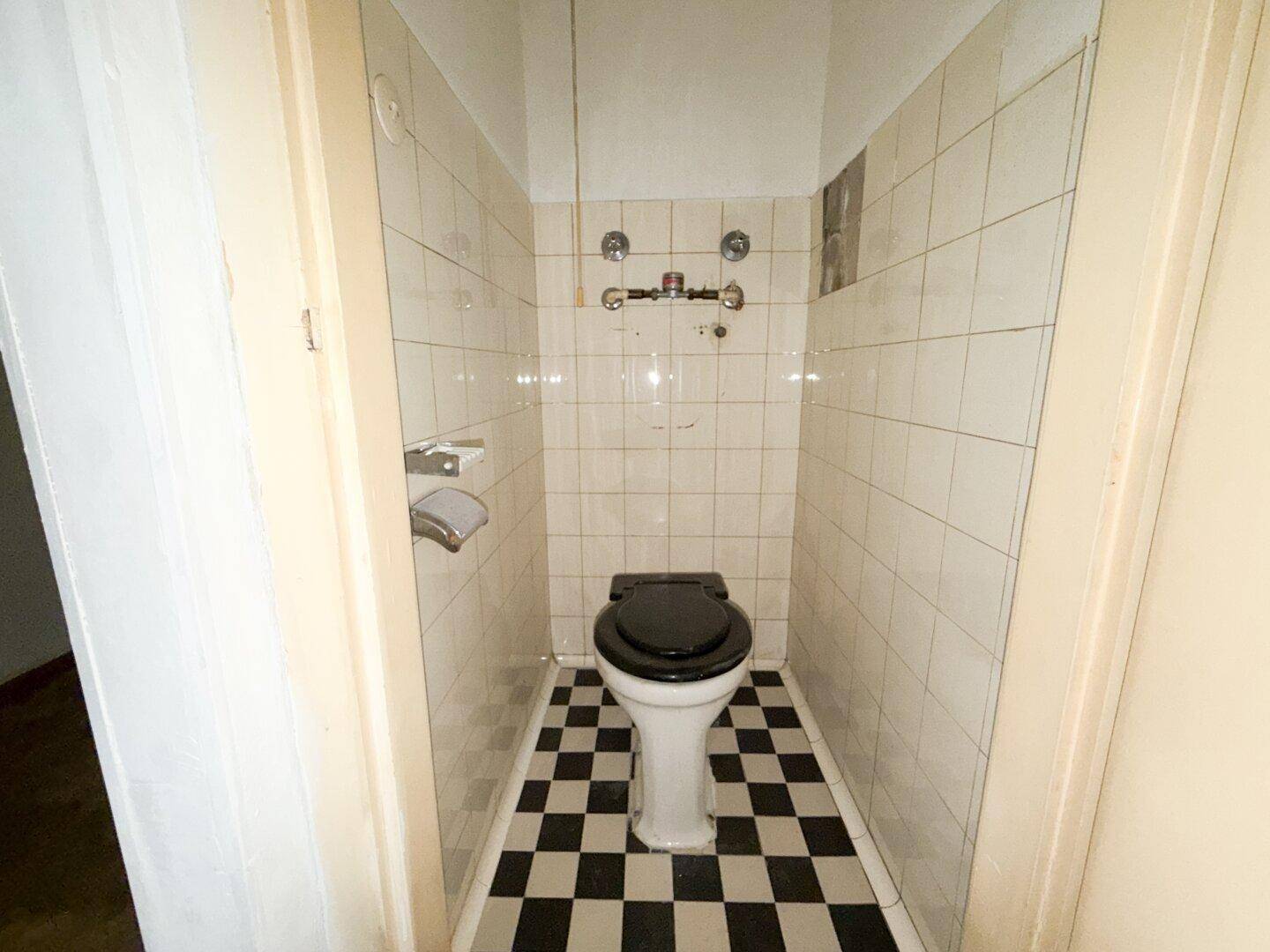 Kleiner Toilettenraum mit schwarz-weiß kariertem Boden und weißen Fliesen, ausgestattet mit einer Toilette.