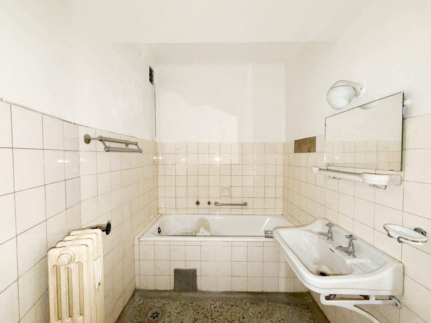 Badezimmer mit Badewanne, Waschbecken und weißen Fliesen, das eine Renovierung benötigt.
