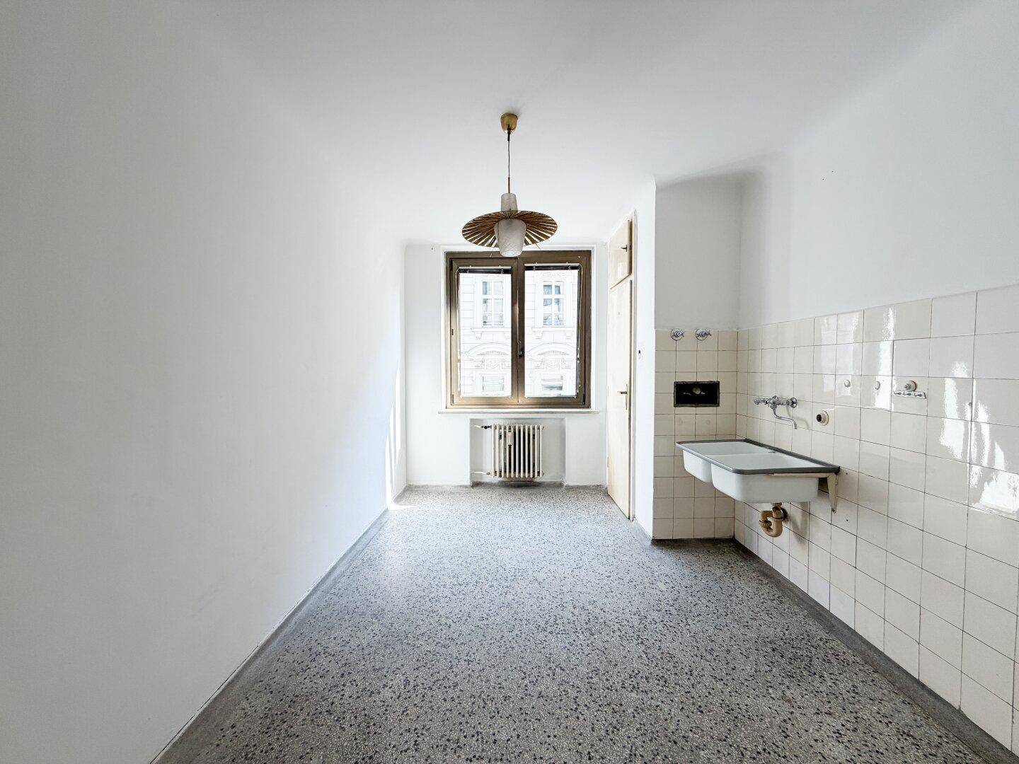 Leere Küche mit Fenster, Heizkörper und gefliestem Bereich, bereit für eine neue Einrichtung.