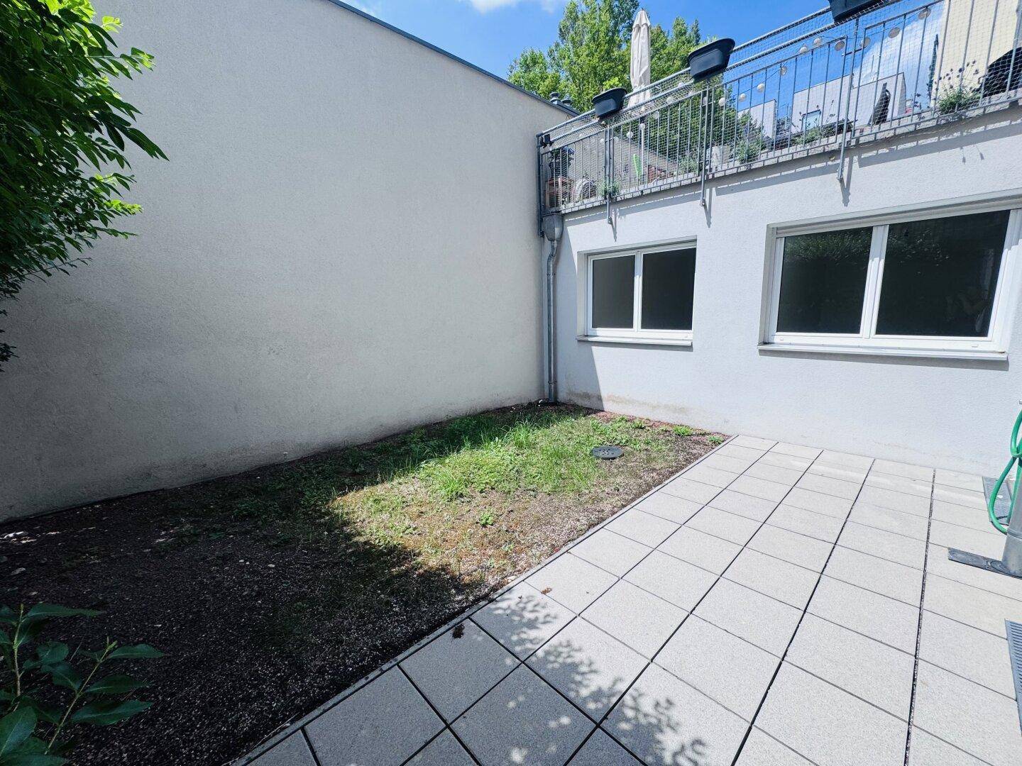 Unmöblierte Terrasse mit einem kleinen, noch nicht vollständig begrünten Gartenbereich neben der Hauswand.