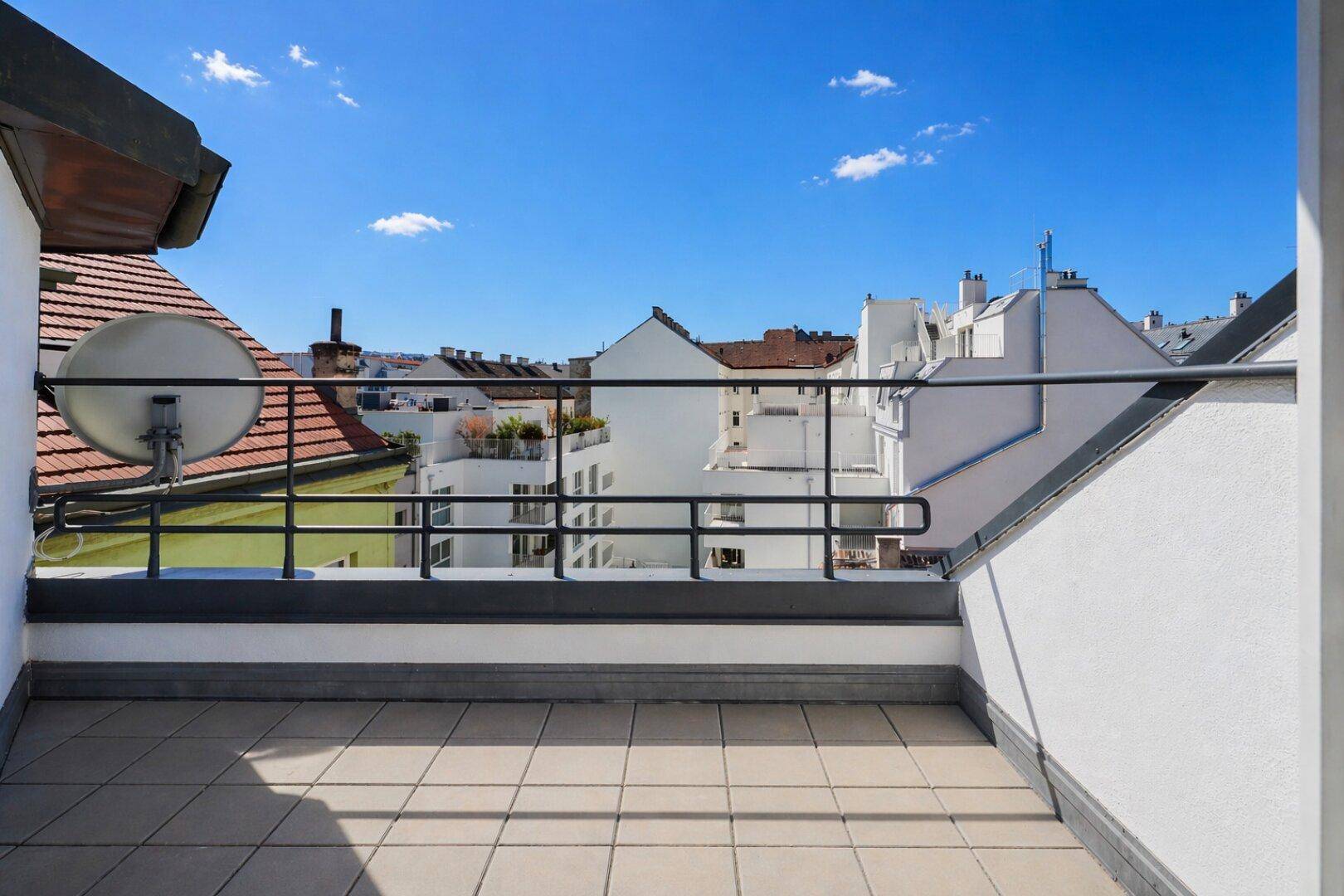 Unmöblierte Dachterrasse mit Fliesenboden und weitem Blick über die umliegenden Dächer der Stadt.