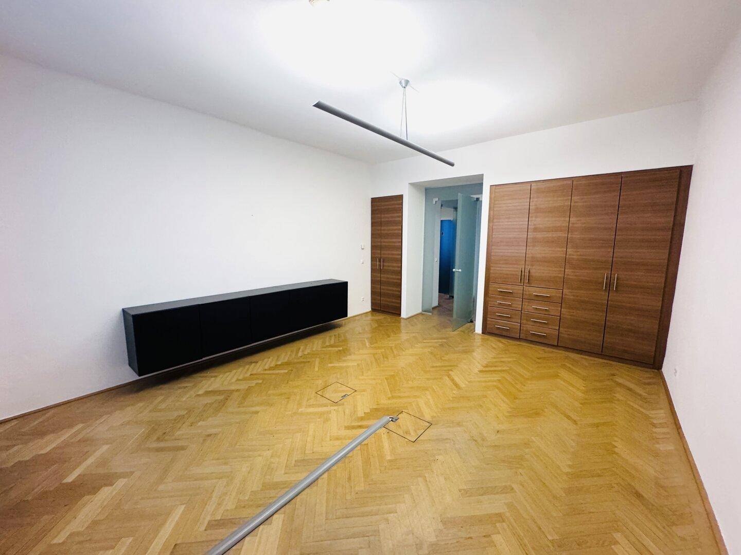 Bürofläche mit Fischgrätparkett, eleganten Holzschränken und einem langen schwarzen Sideboard.