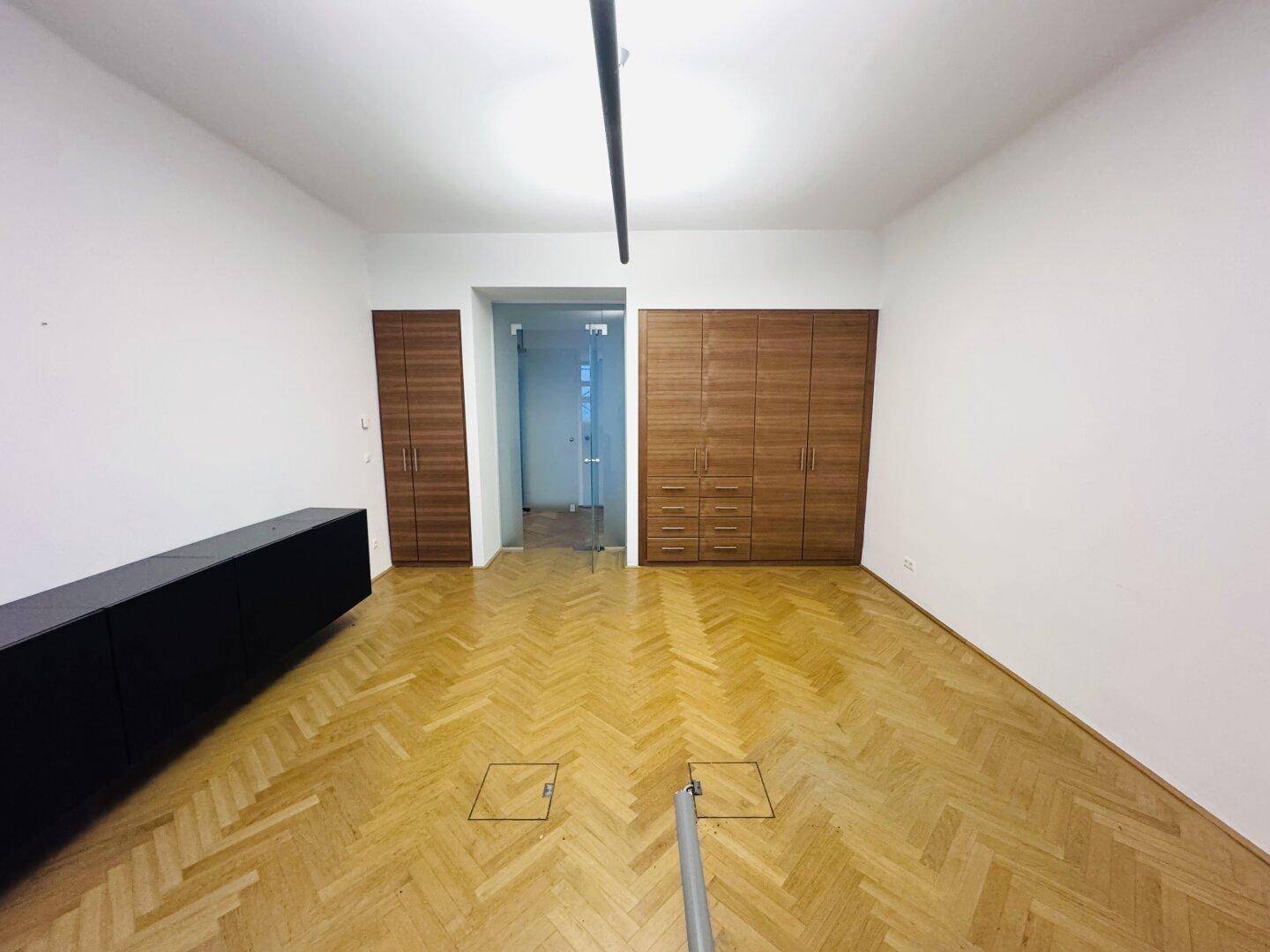 Geräumiger Büroraum mit Fischgrätparkett, integrierten Holzschränken und einem modernen Sideboard.