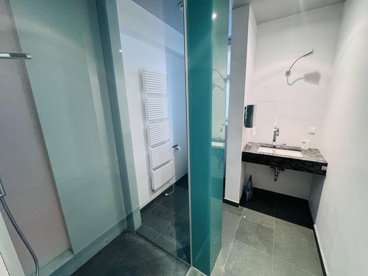 Modernes Badezimmer mit dunklen Fliesen, Glasdusche, Handtuchwärmer und Marmorwaschtisch.