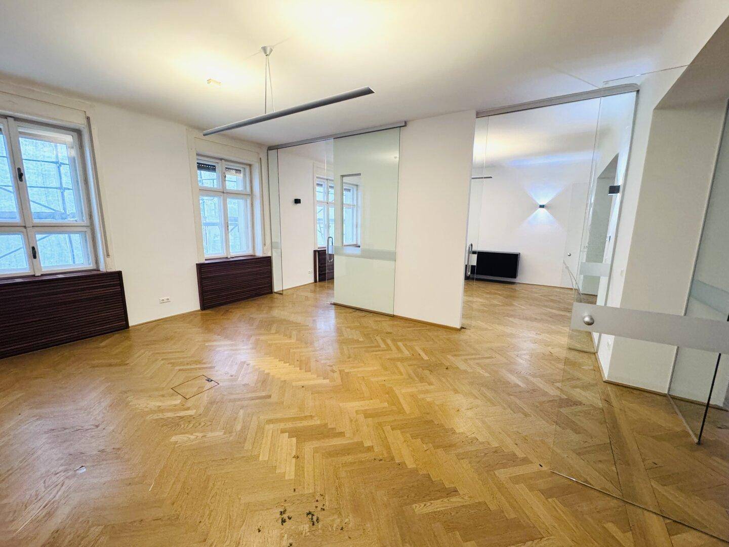 Geräumiger Bürobereich mit Fischgrätparkett, modernen Glasabtrennungen und viel Tageslicht.