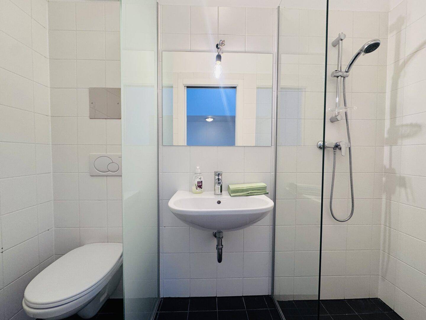 Modernes Badezimmer mit weißen Wandfliesen, dunklen Bodenfliesen, wandhängendem WC und Dusche.