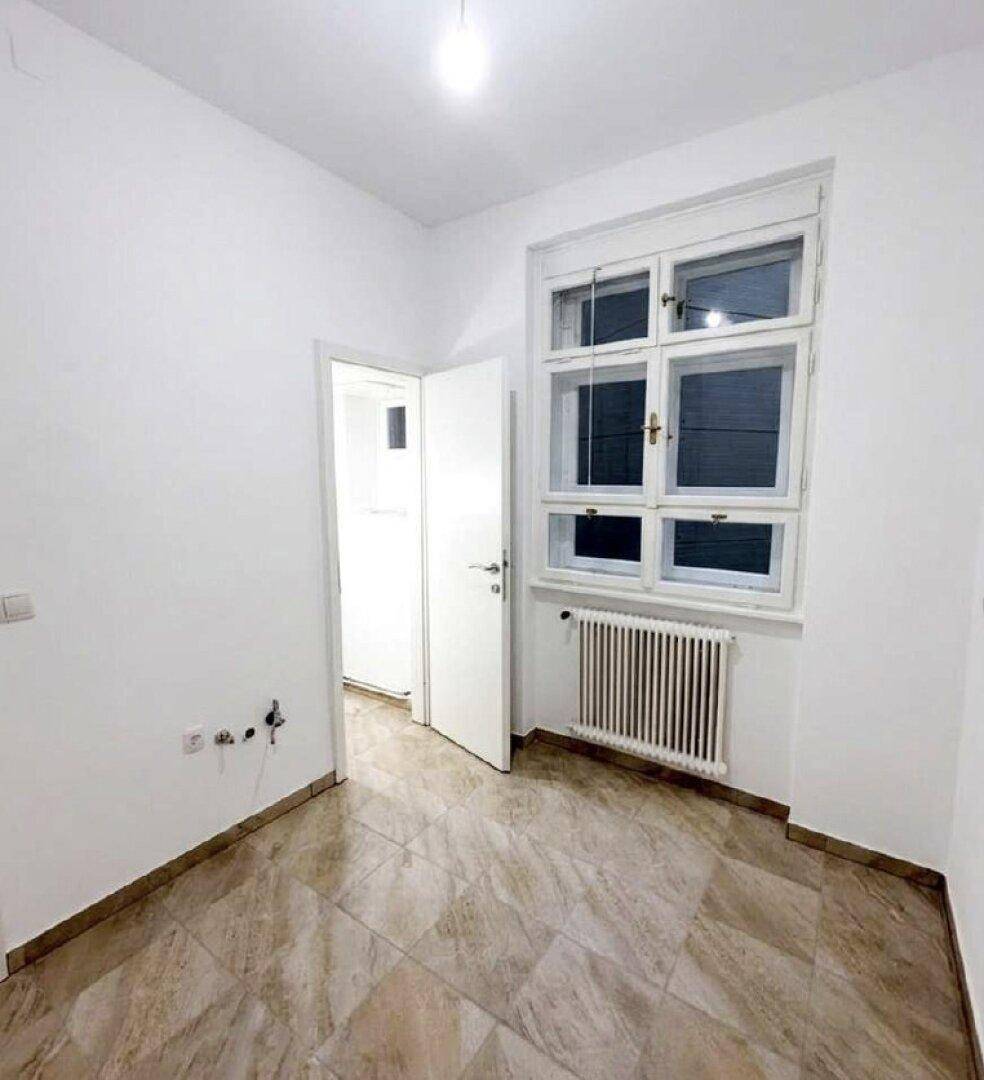Kleiner Raum mit Fliesenboden, Fenster und Heizkörper, ideal als Arbeits- oder Gästezimmer.