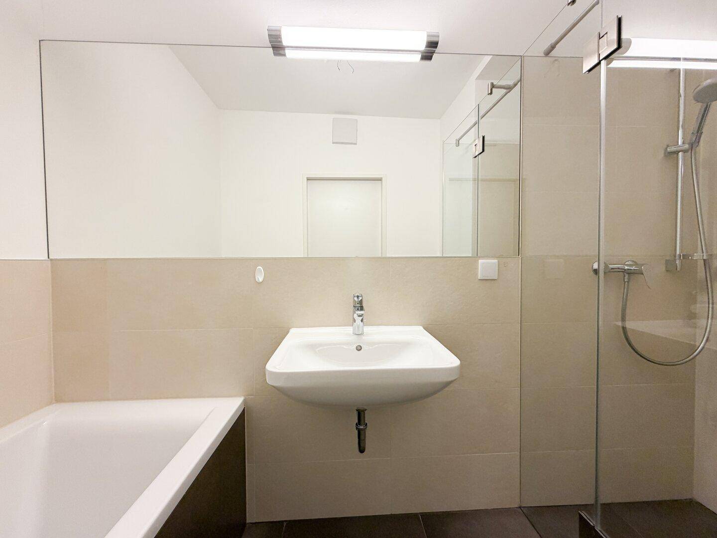 Modernes Badezimmer mit Badewanne, begehbarer Dusche, großem Spiegel und eleganten beigefarbenen Fliesen.