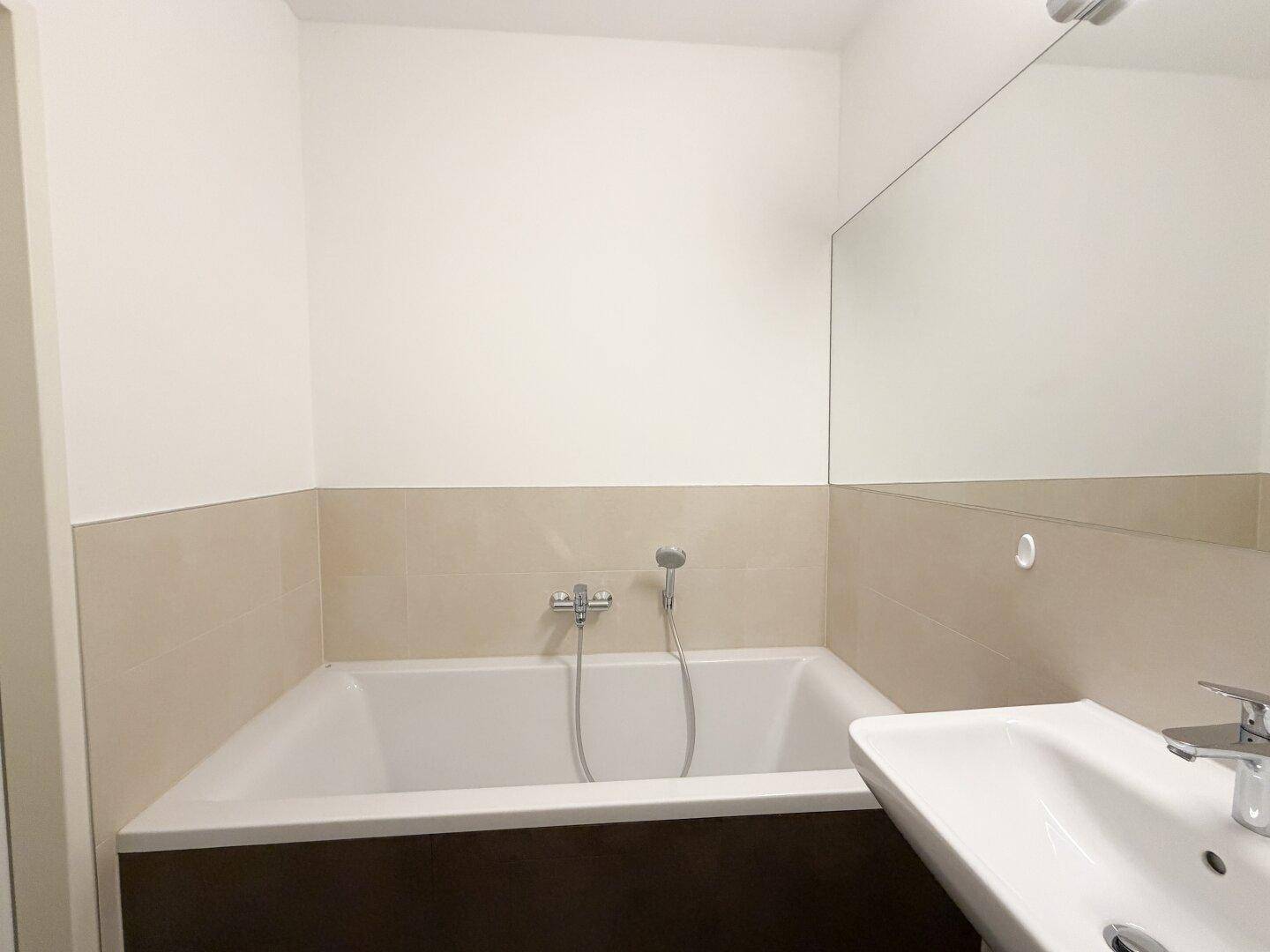 Elegantes Badezimmer mit integrierter Badewanne und modernem Waschbecken, umgeben von hellen Fliesen.