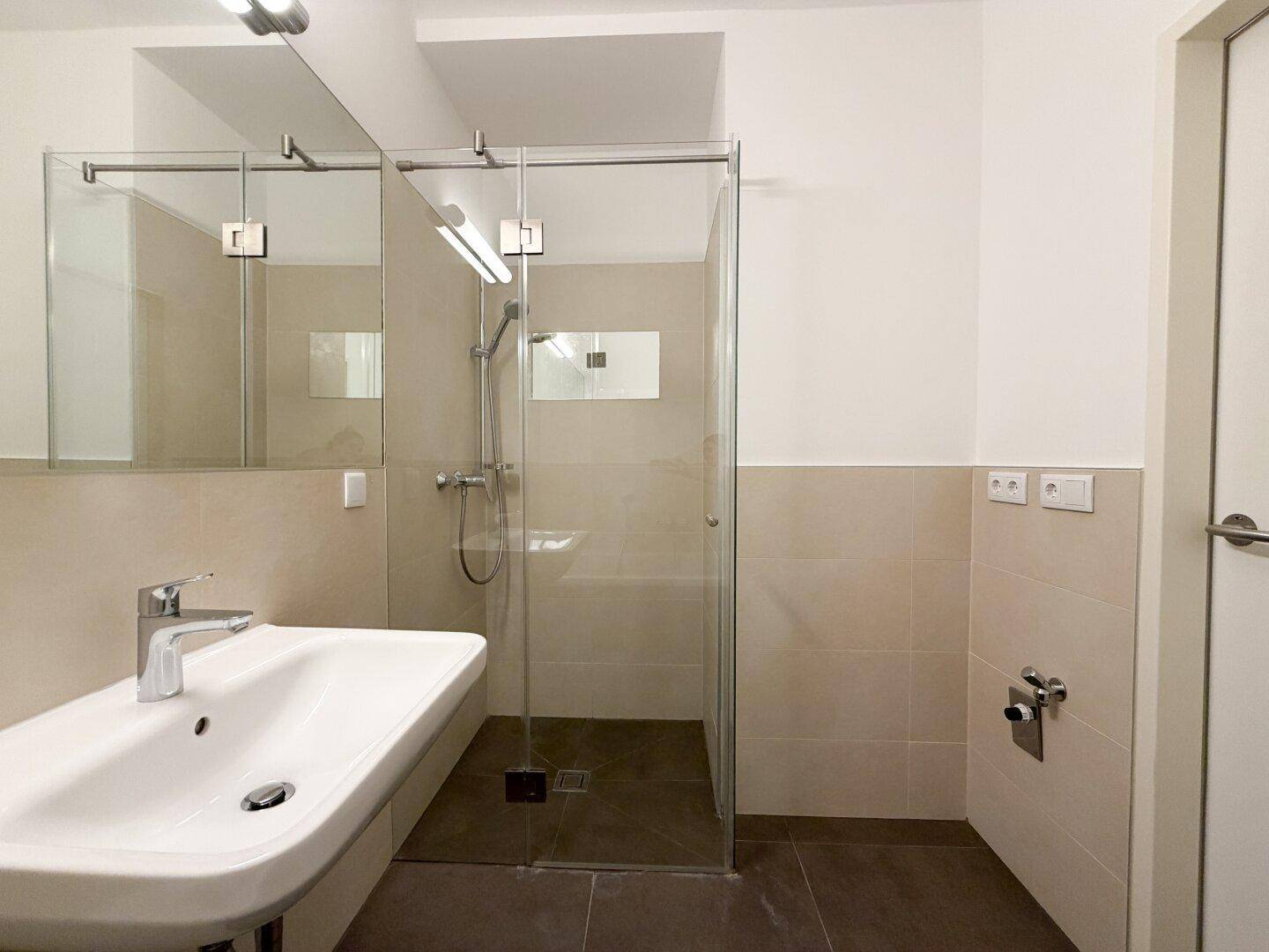 Helles Badezimmer mit modernem Waschbecken, großem Spiegel und einer geräumigen begehbaren Dusche.