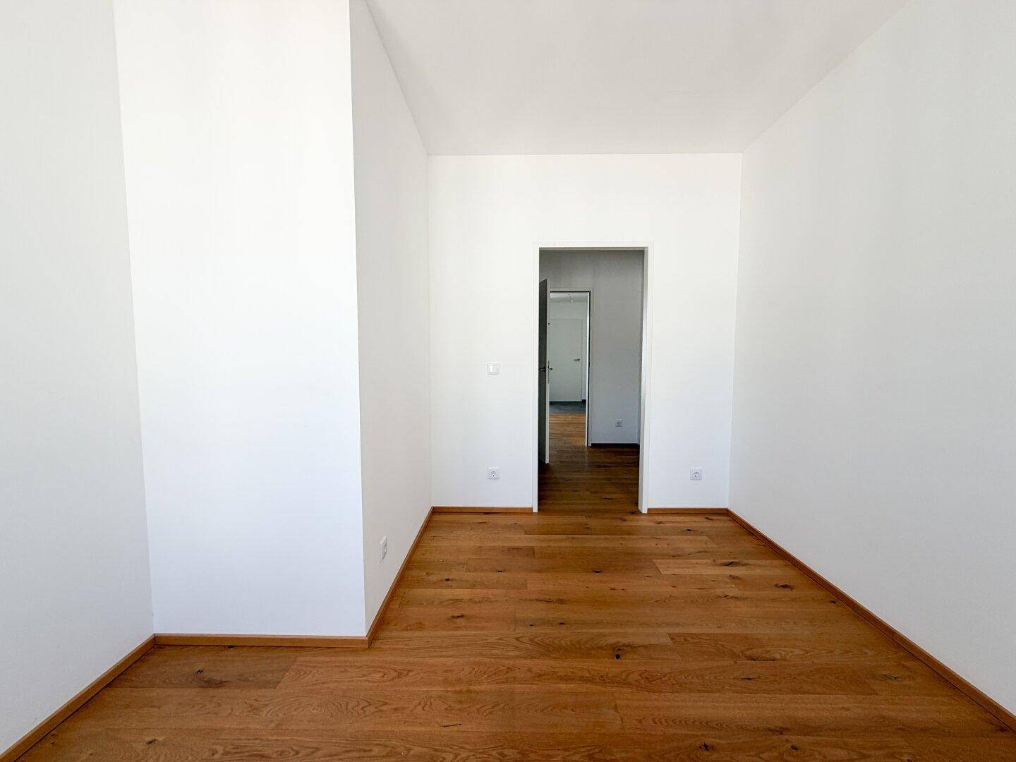 Heller Raum mit Holzboden und weiß gestrichenen Wänden, ideal als Schlaf- oder Arbeitszimmer nutzbar.