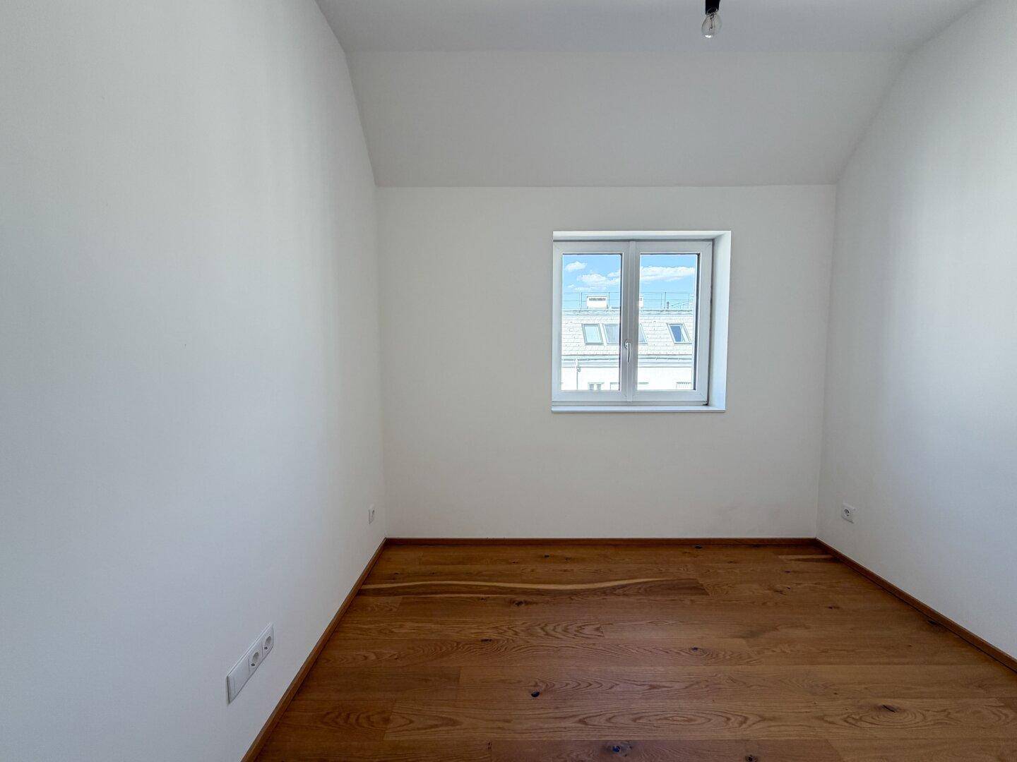 Ruhiges Zimmer mit Holzboden und einem Fenster, das den Raum mit natürlichem Licht erfüllt.