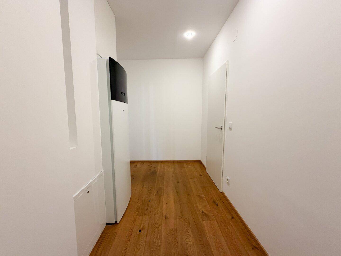 Heller Flur mit Holzboden und weiß gestrichenen Wänden, ausgestattet mit einer modernen Heizungsanlage.