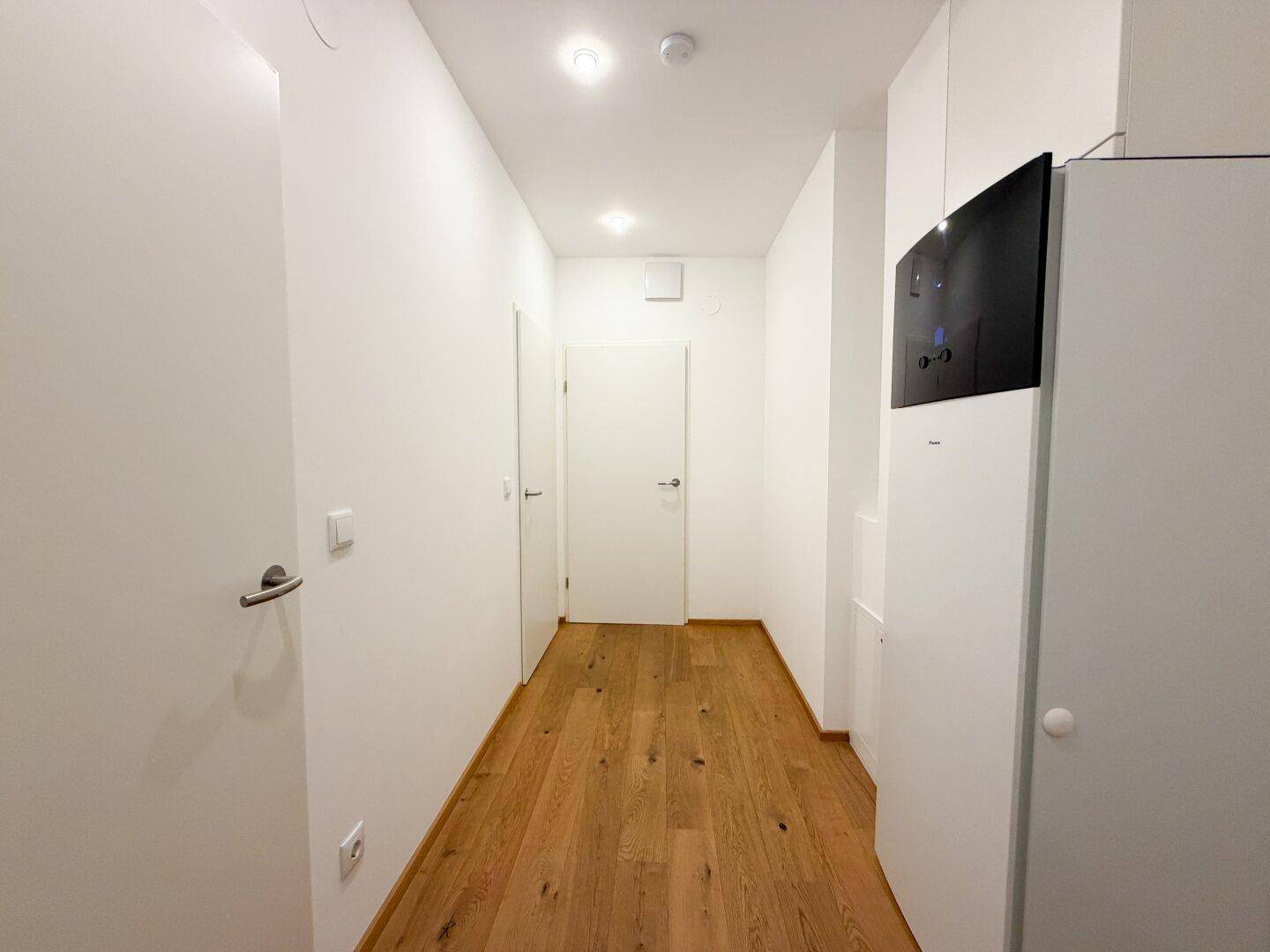 Langer, heller Flur mit Holzboden und mehreren Türen, der verschiedene Räume miteinander verbindet.