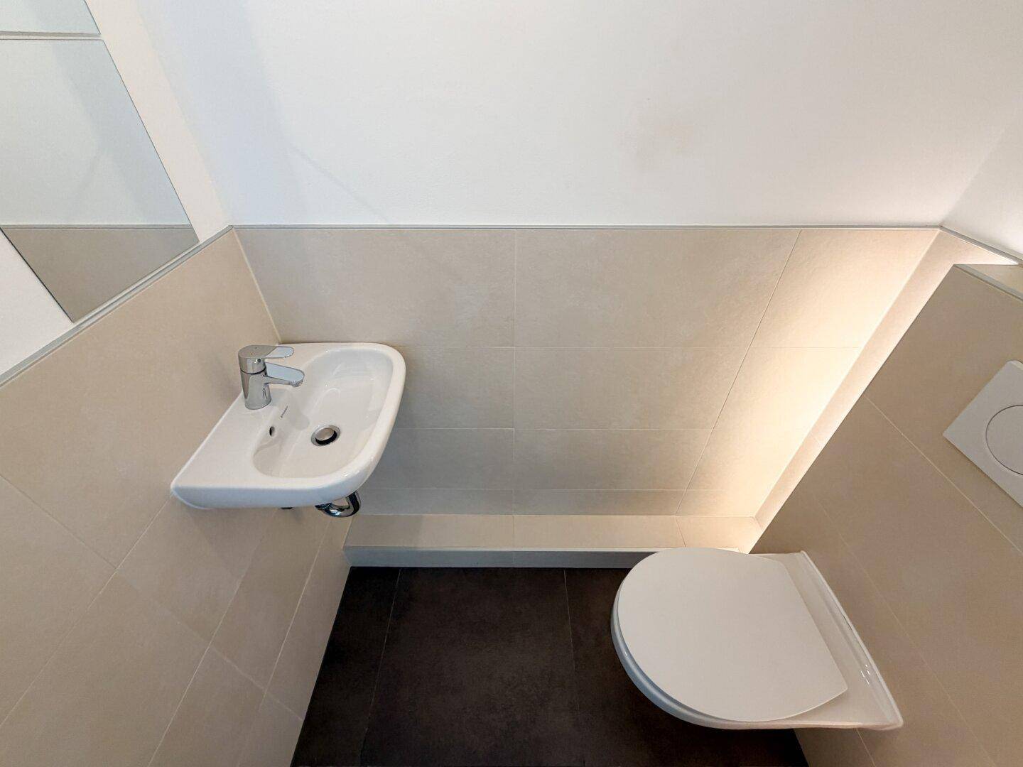 Kompaktes Gäste-WC mit wandhängender Toilette und kleinem Waschbecken unter einer Dachschräge.