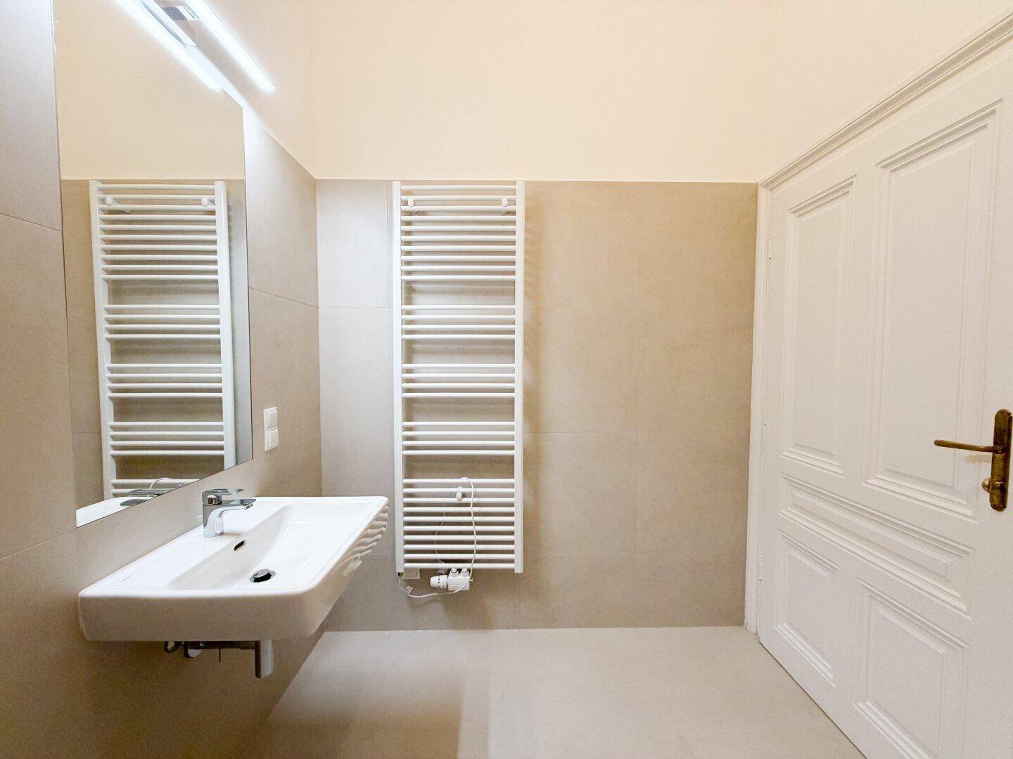 Modernes Badezimmer mit Waschbecken, Spiegel und beheiztem Handtuchhalter, alles in neutralen Tönen.