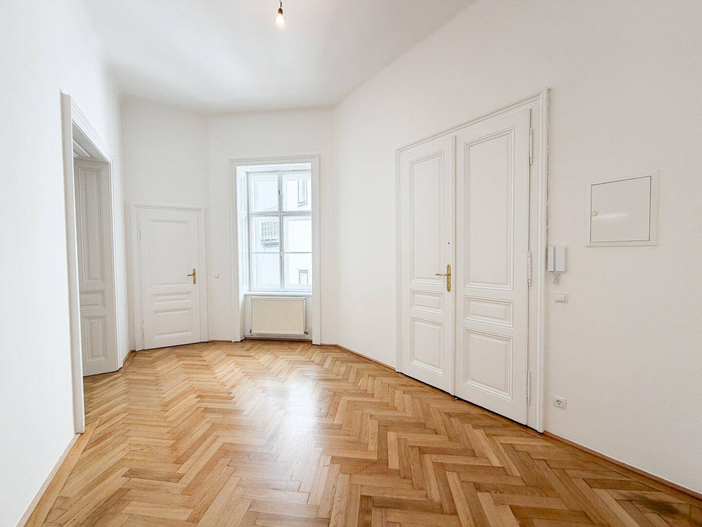 Geräumiger Flur mit Fischgrätparkett, hohen Türen und Gegensprechanlage, der den Eingangsbereich bildet.