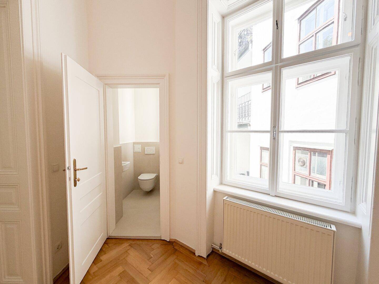 Heller Raum mit Fischgrätparkett und Zugang zu einem separaten WC mit modernem Design.