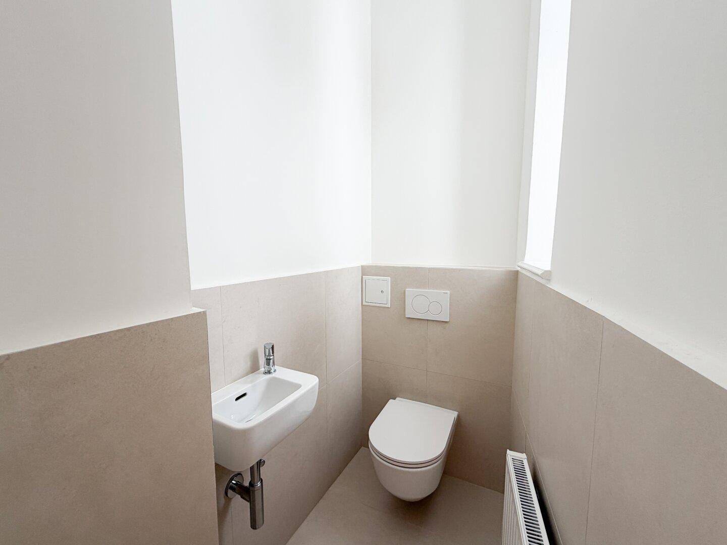 Modernes Gäste-WC mit wandhängender Toilette, kleinem Waschbecken und hellen Fliesen.