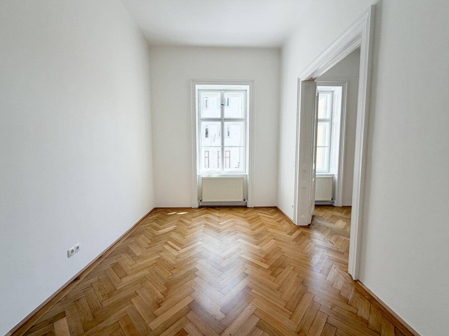 Gemütliches Zimmer mit Fischgrätparkett und einem großen Fenster, ideal als Schlaf- oder Arbeitszimmer.