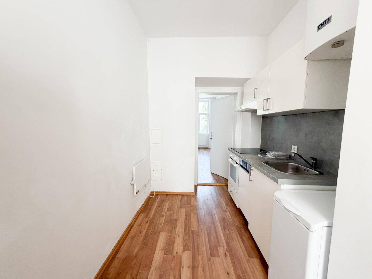 Kleine, funktionale Küche mit weißen Schränken, grauer Rückwand und Laminatboden.