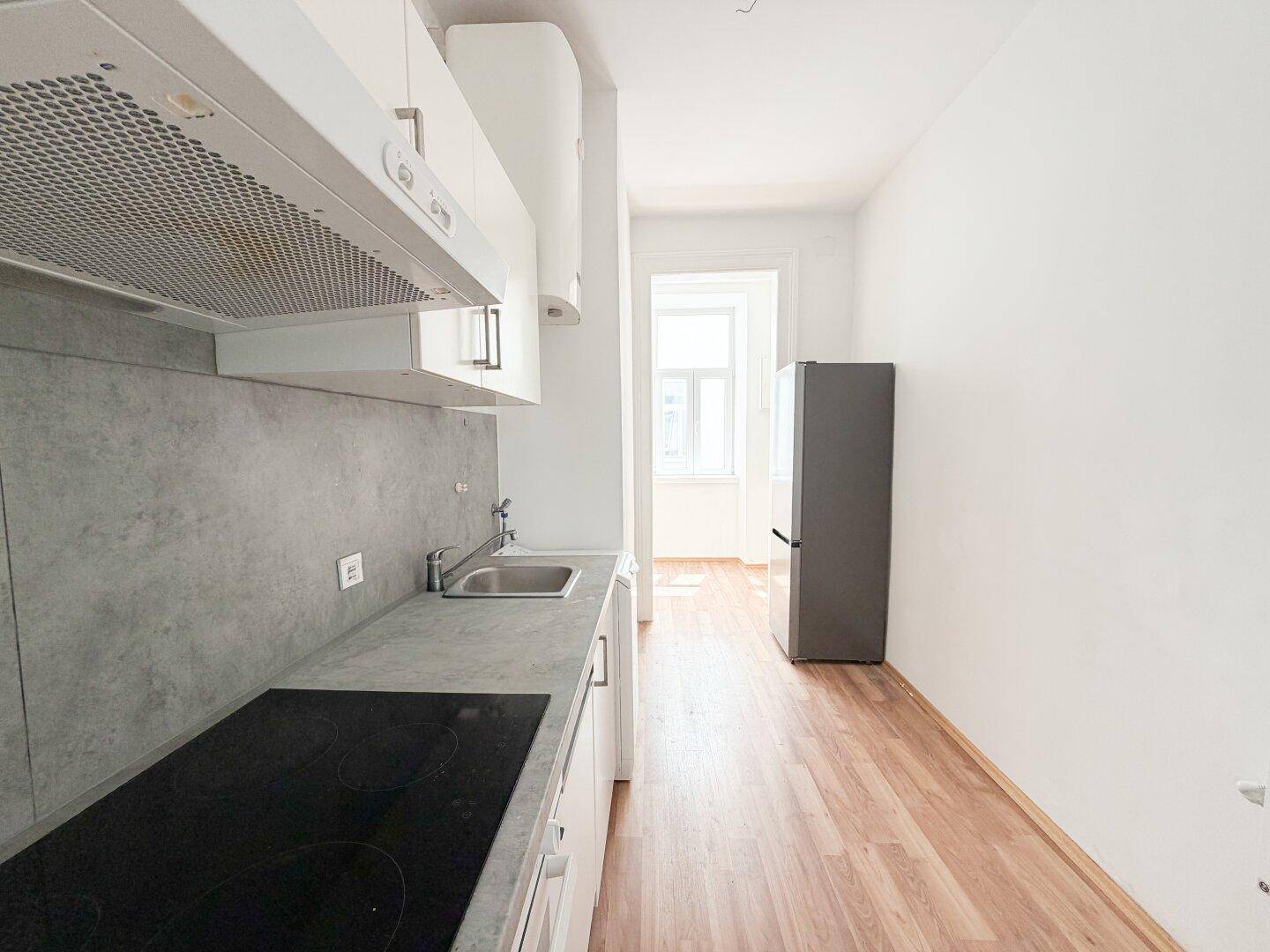 Moderne Küchenzeile mit weißen Schränken, Induktionskochfeld, Backofen und Kühlschrank.