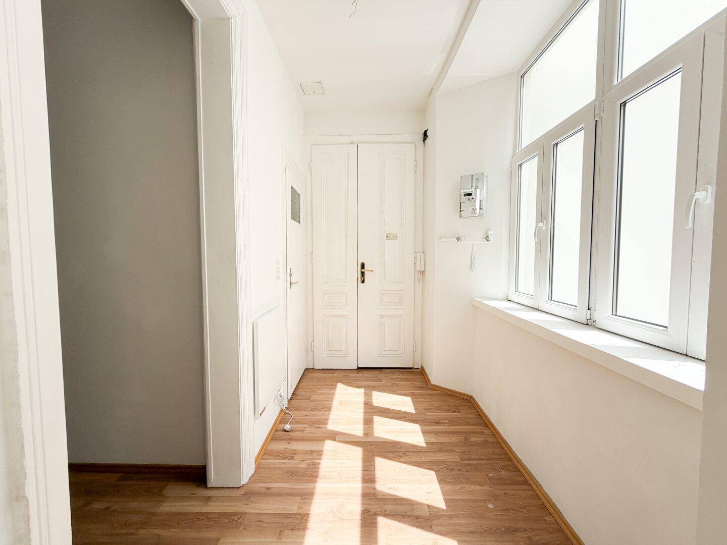 Heller Flur mit Laminatboden, weißen Wänden und einem großen Fenster, das viel Licht hereinlässt.