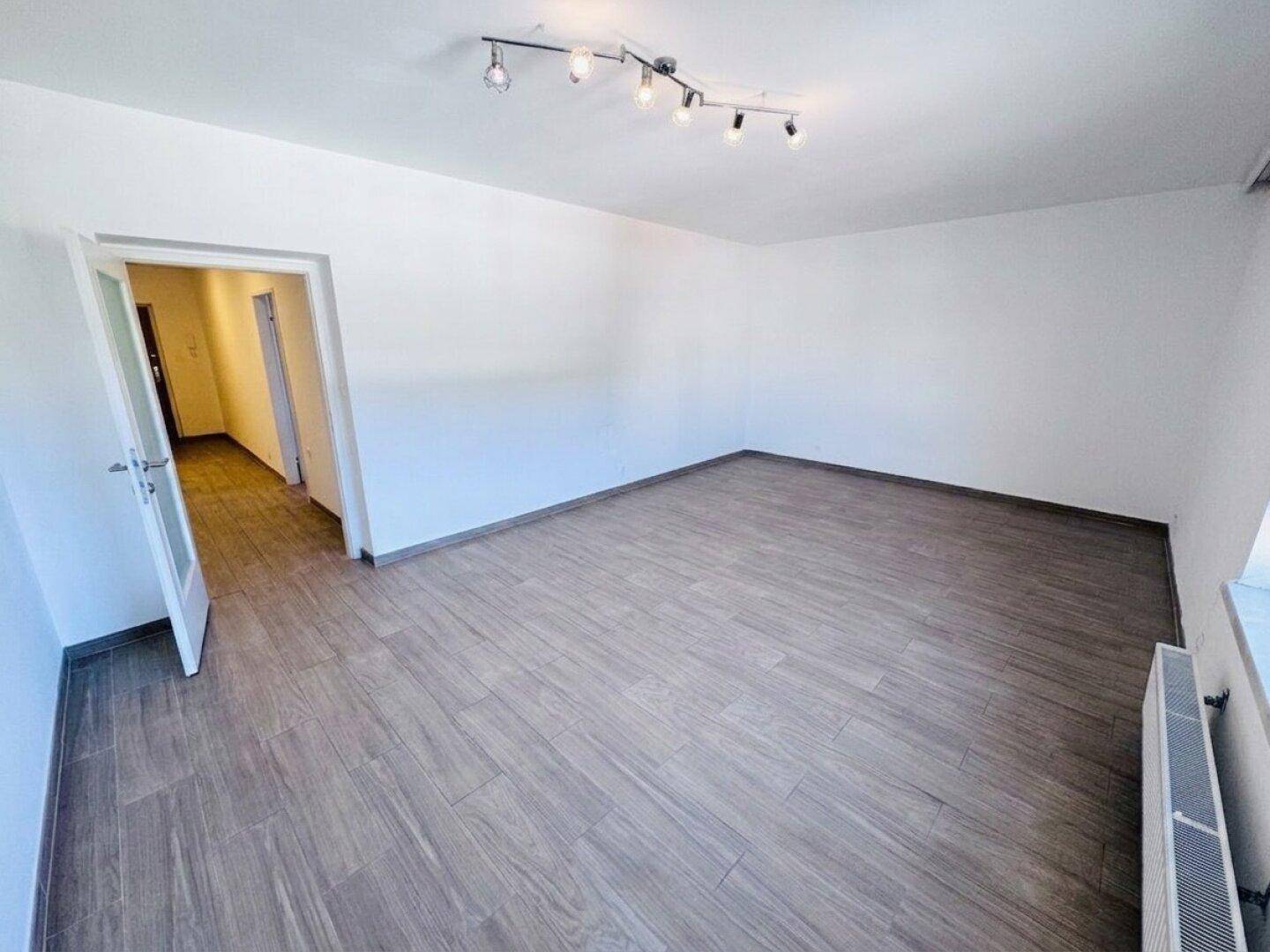Geräumiges, leeres Zimmer mit Laminatboden und Zugang zu einem Flur.