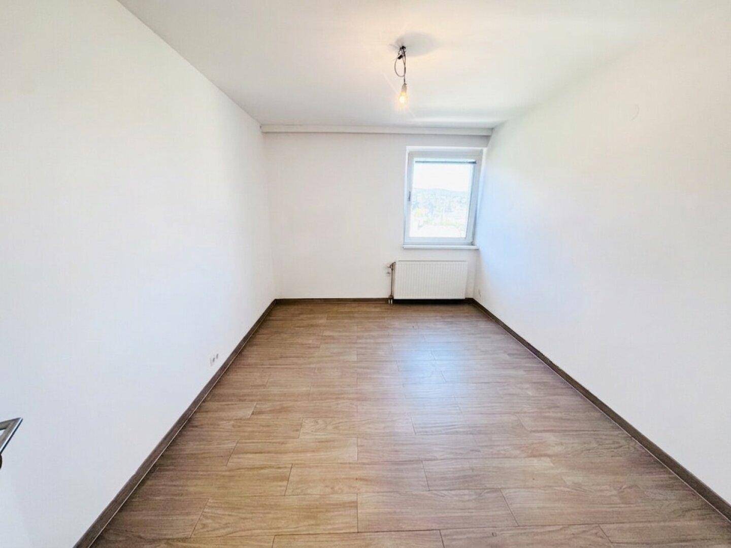 Leeres Schlafzimmer mit hellem Laminatboden und weiß gestrichenen Wänden.