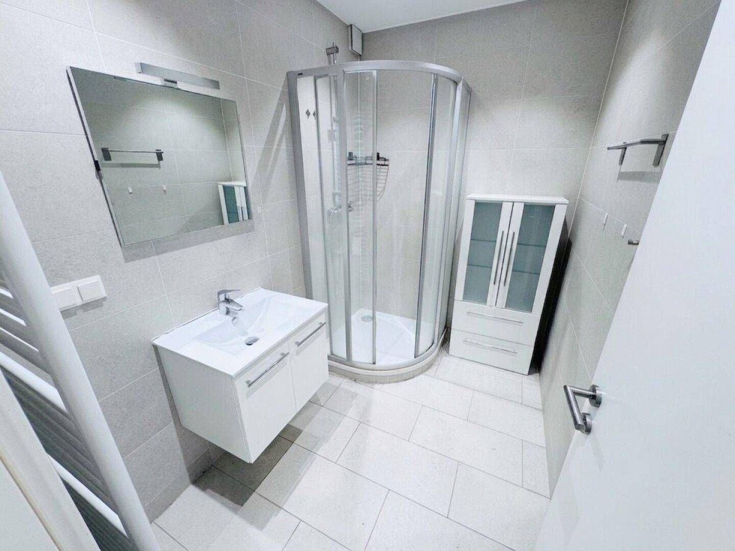 Modernes Badezimmer mit grauen Fliesen, Eckdusche und Waschtisch mit Unterschrank.