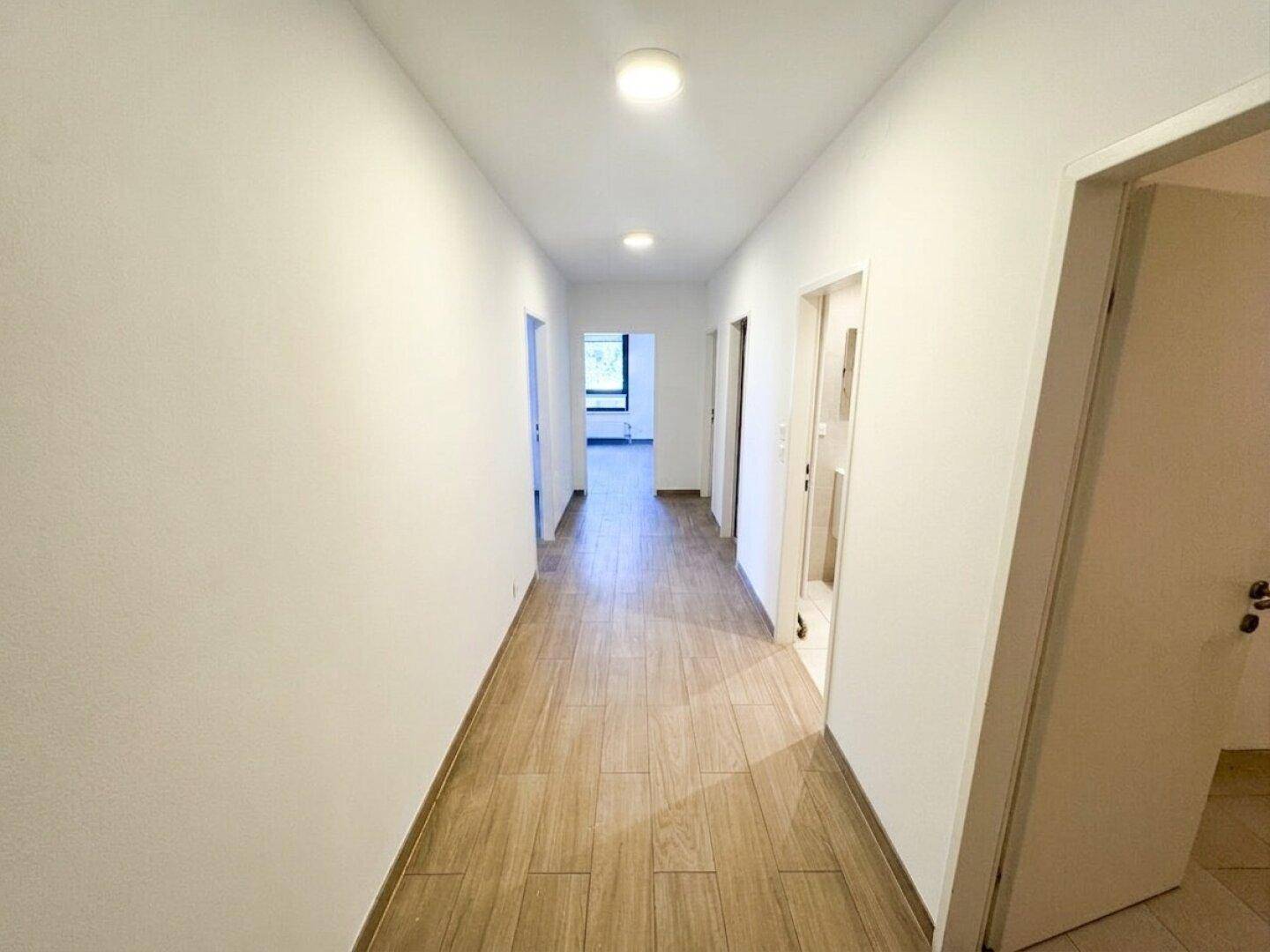 Langer, heller Flur mit modernem Laminatboden und mehreren Türen.