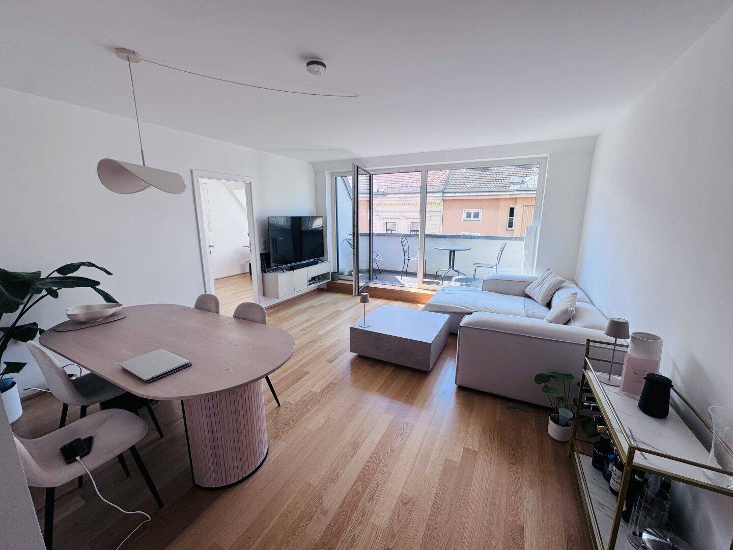 Heller Wohn- und Essbereich mit Holzboden, modernem Mobiliar und Zugang zu einem Balkon.