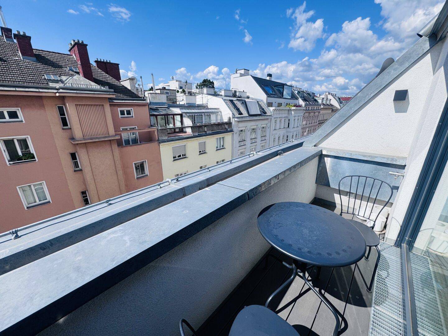 Kleiner Balkon mit Sitzgelegenheiten und einem Ausblick auf die umliegenden Stadtgebäude.
