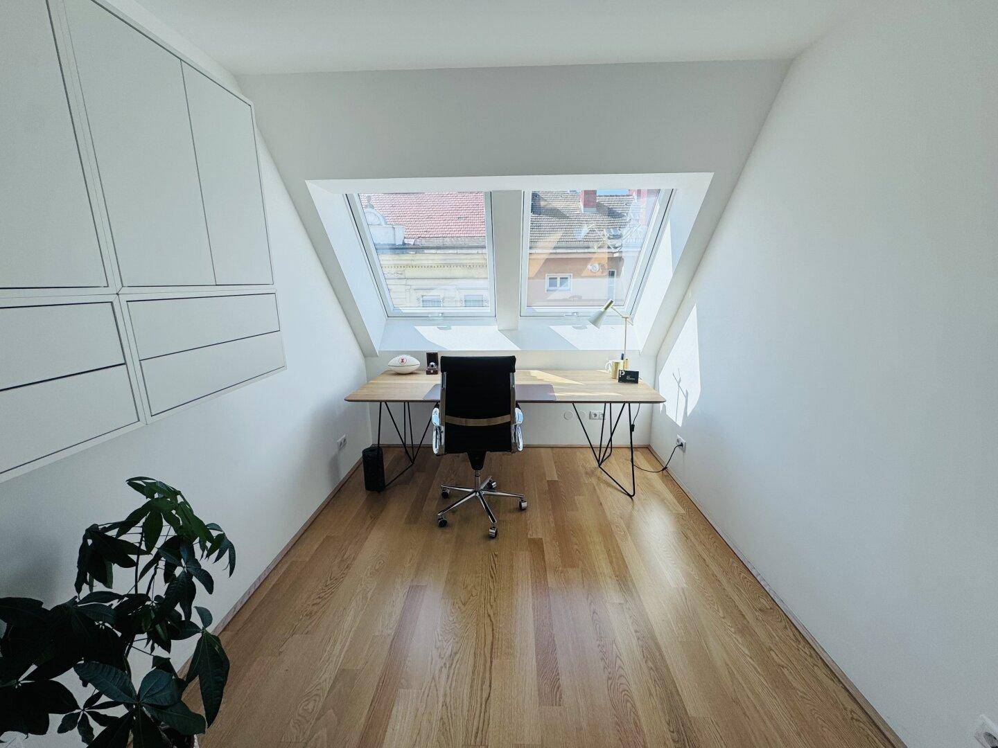 Helles Arbeitszimmer mit Schreibtisch, Einbauschränken und Dachfenstern im Dachgeschoss.