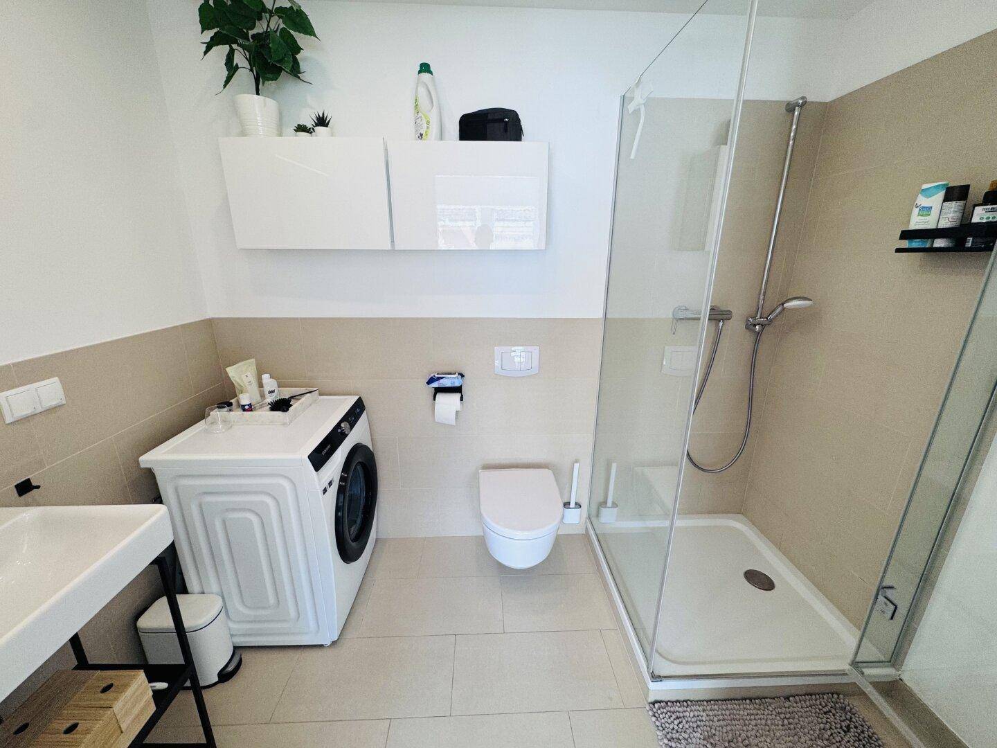 Modernes Badezimmer mit Duschkabine, Toilette, Waschbecken und integrierter Waschmaschine.