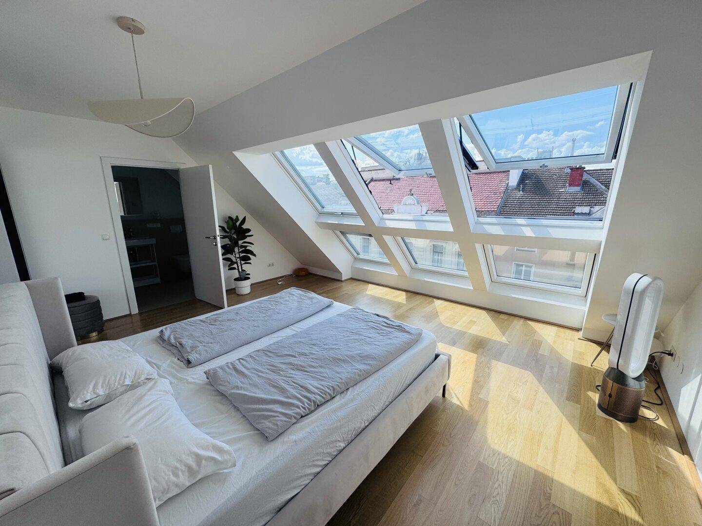 Schlafzimmer im Dachgeschoss mit großzügigen Dachfenstern, Holzboden und Blick über die Stadt.