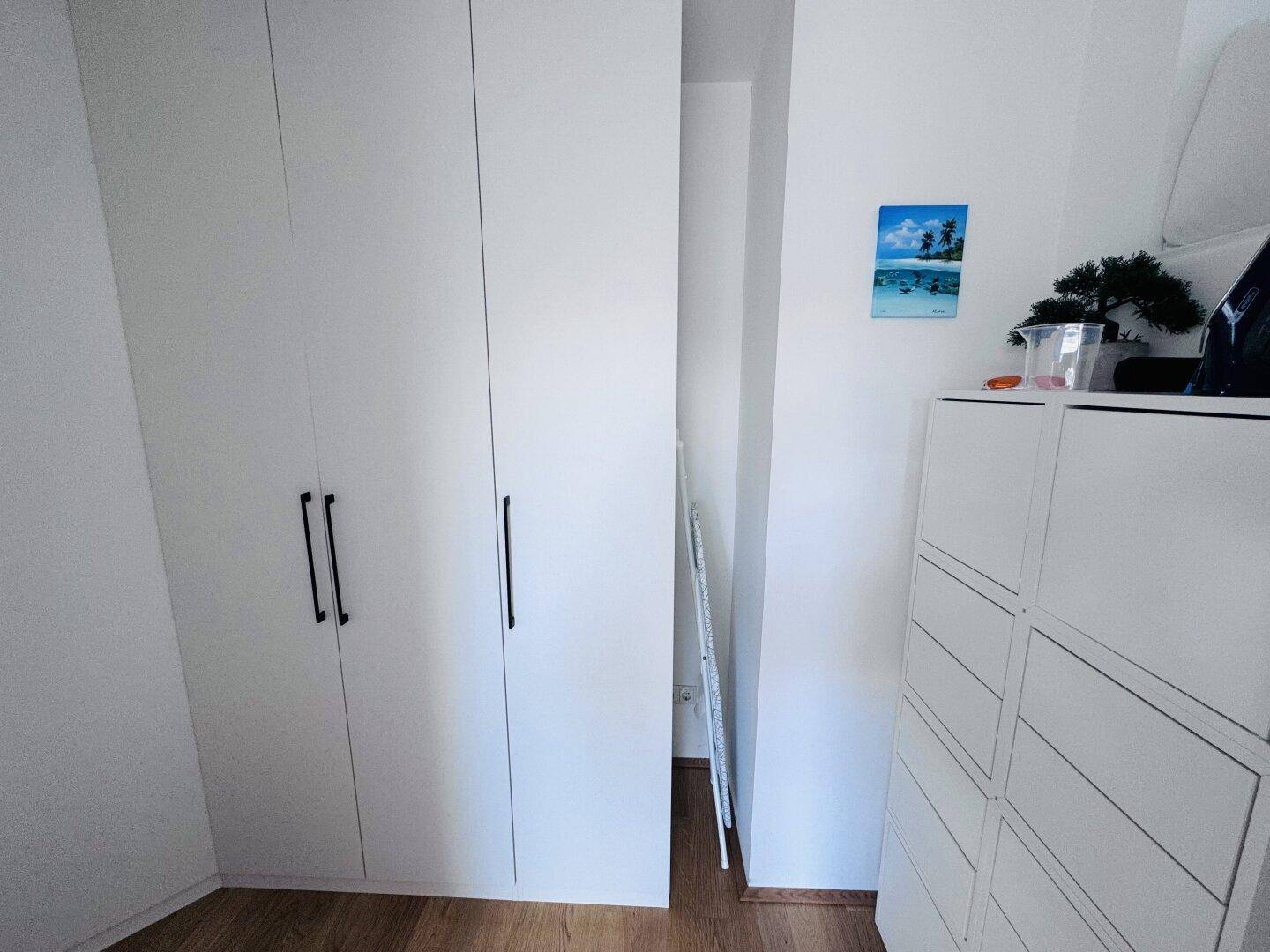 Praktischer Stauraum mit weißen Einbauschränken und Kommode auf Holzboden.