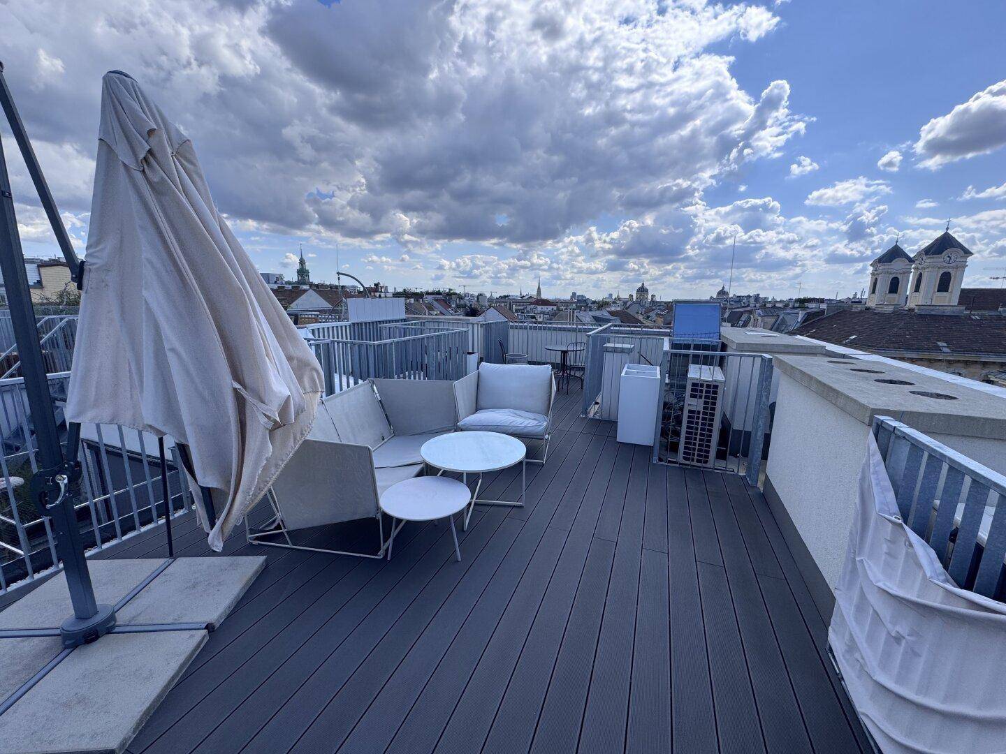Große Dachterrasse mit Lounge-Möbeln, Sonnenschirm und weitem Panoramablick über die Stadt.