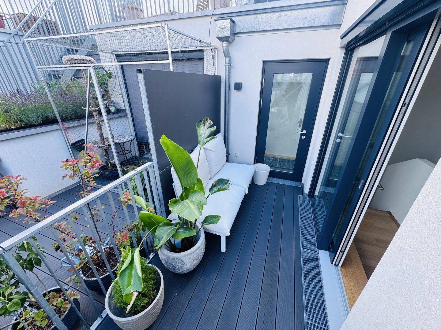 Kleiner Balkon mit Pflanzen, einer Liege und Zugang zum Innenbereich.