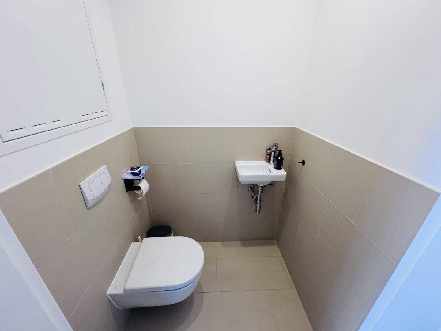 Modernes Gäste-WC mit wandhängender Toilette und kleinem Waschbecken, komplett gefliest.