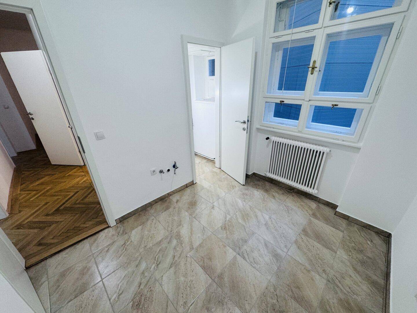 Funktionaler Raum mit Fliesenboden, Fenster und vorbereiteten Anschlüssen für Sanitärinstallationen.