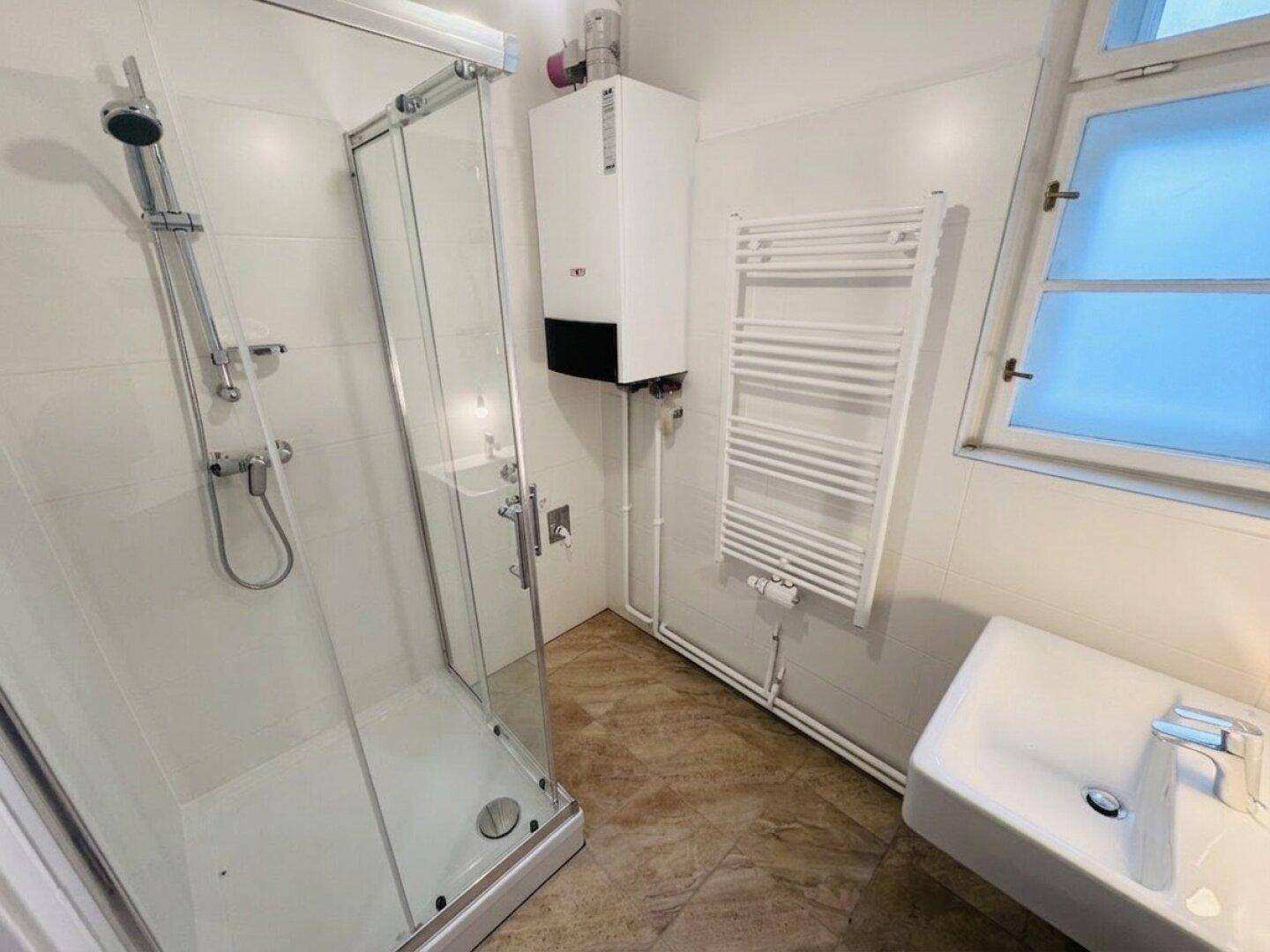 Modernes Badezimmer mit Duschkabine, Waschbecken, beheiztem Handtuchhalter und Fenster.