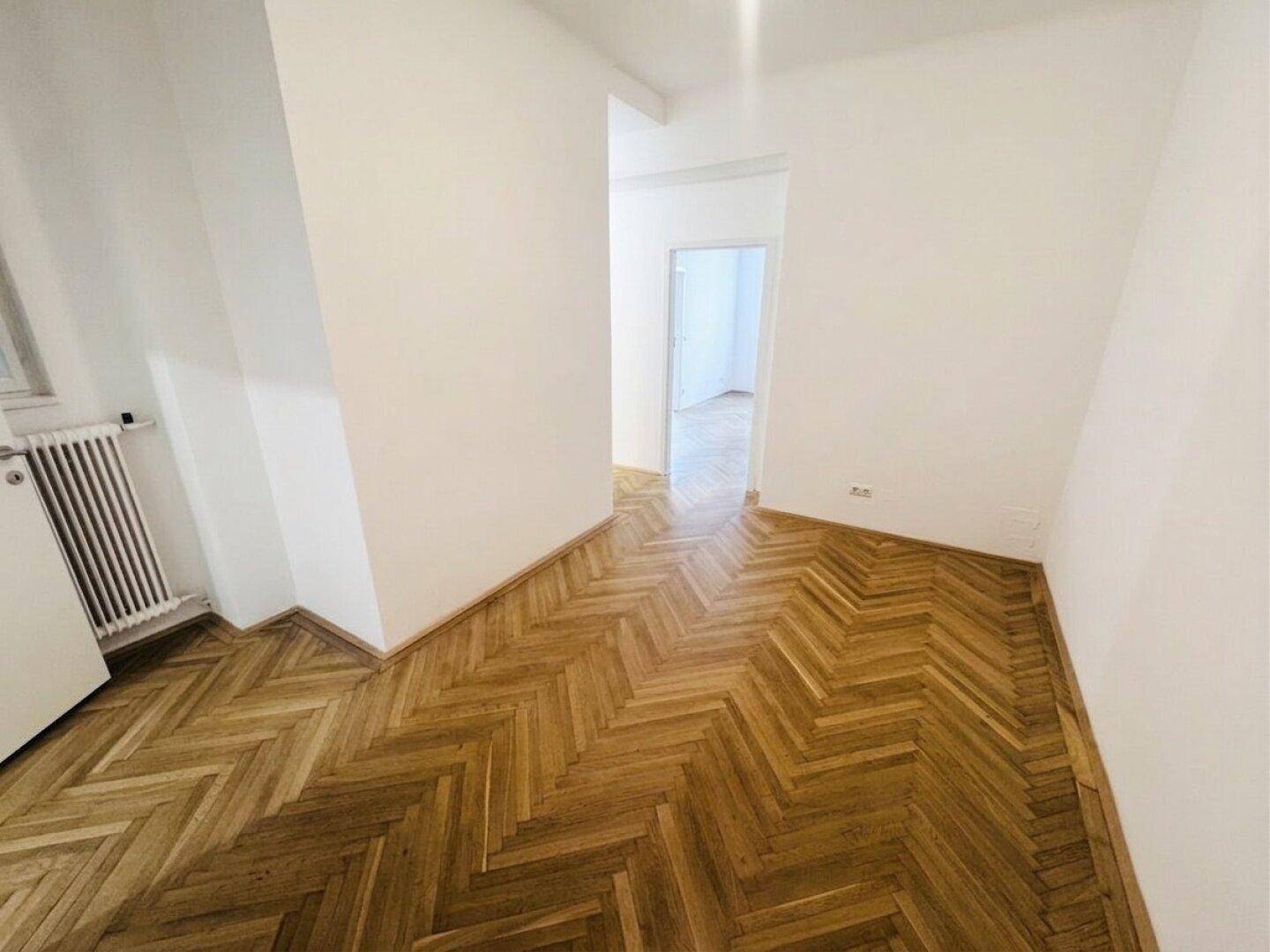 Heller Flur mit durchgehendem Fischgrätparkett, der verschiedene Räume der Wohnung verbindet.