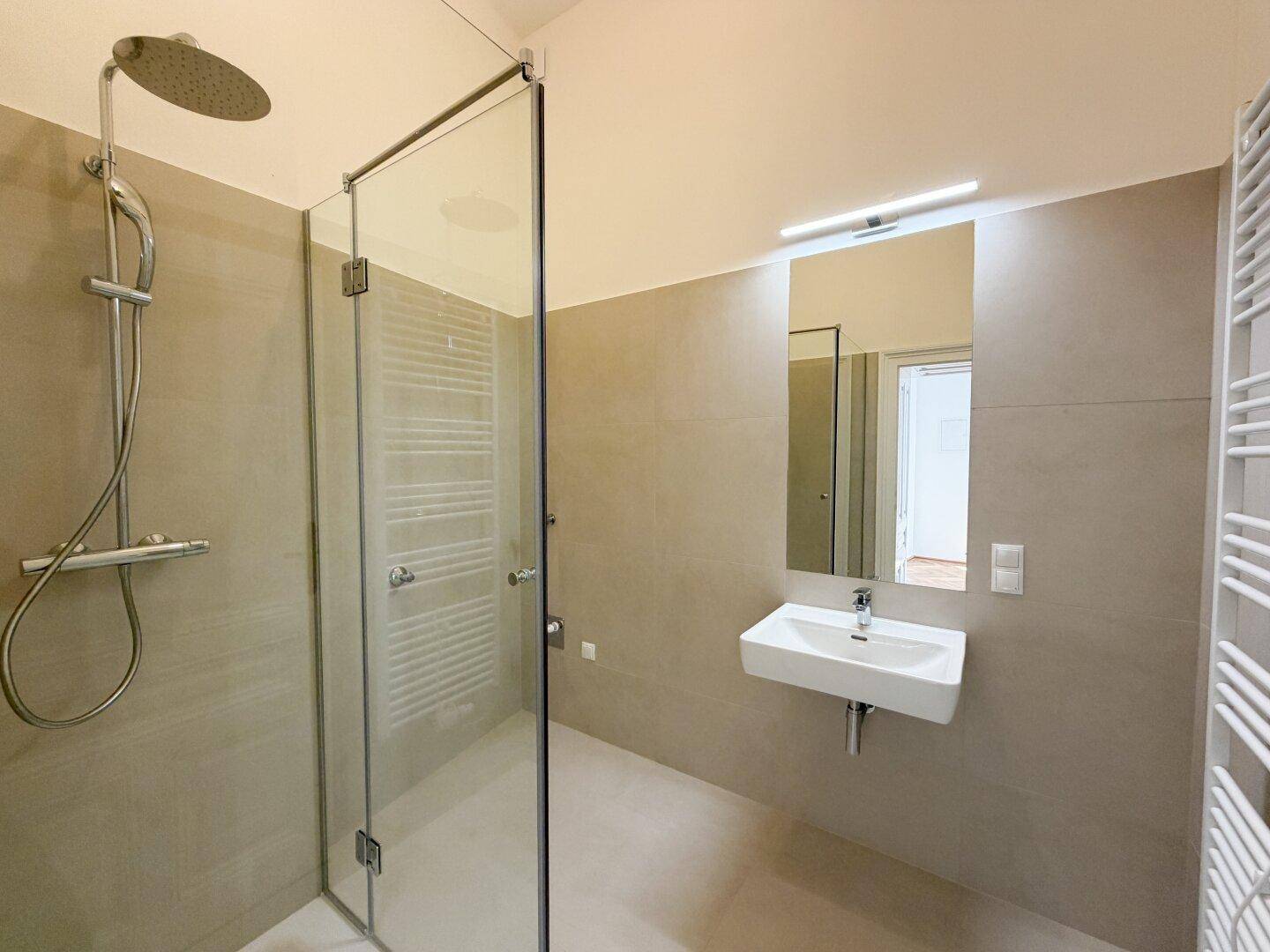 Modernes Badezimmer mit ebenerdiger Dusche, Regenduschkopf, Einzelwaschbecken und beheiztem Handtuchhalter.