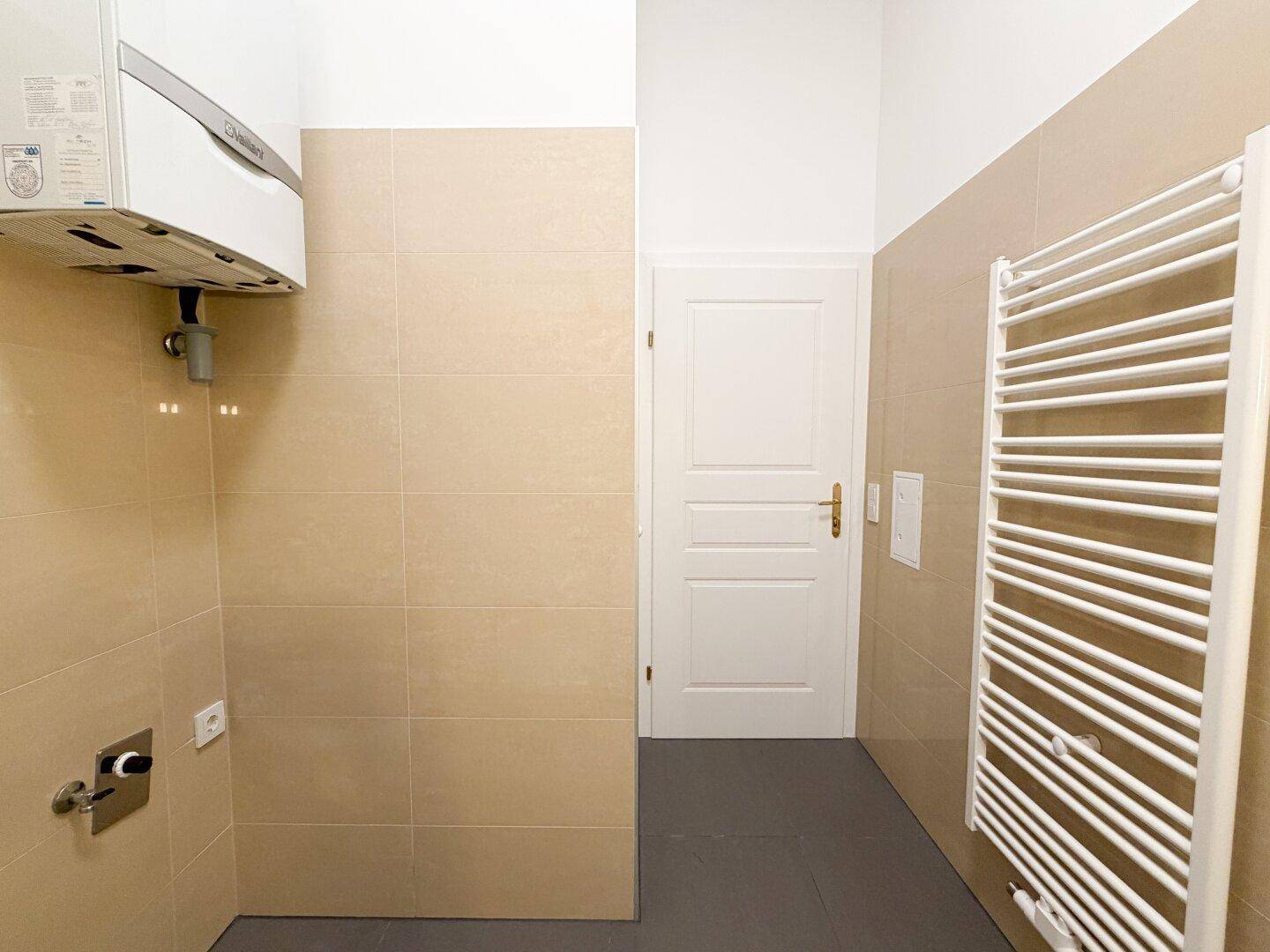 Funktionales Badezimmer mit beigen Fliesen, beheiztem Handtuchhalter und weißer Tür.