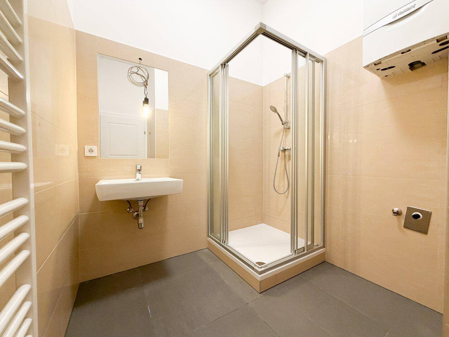 Helles Badezimmer mit beigen Wandfliesen, Duschkabine und modernem Waschbecken.