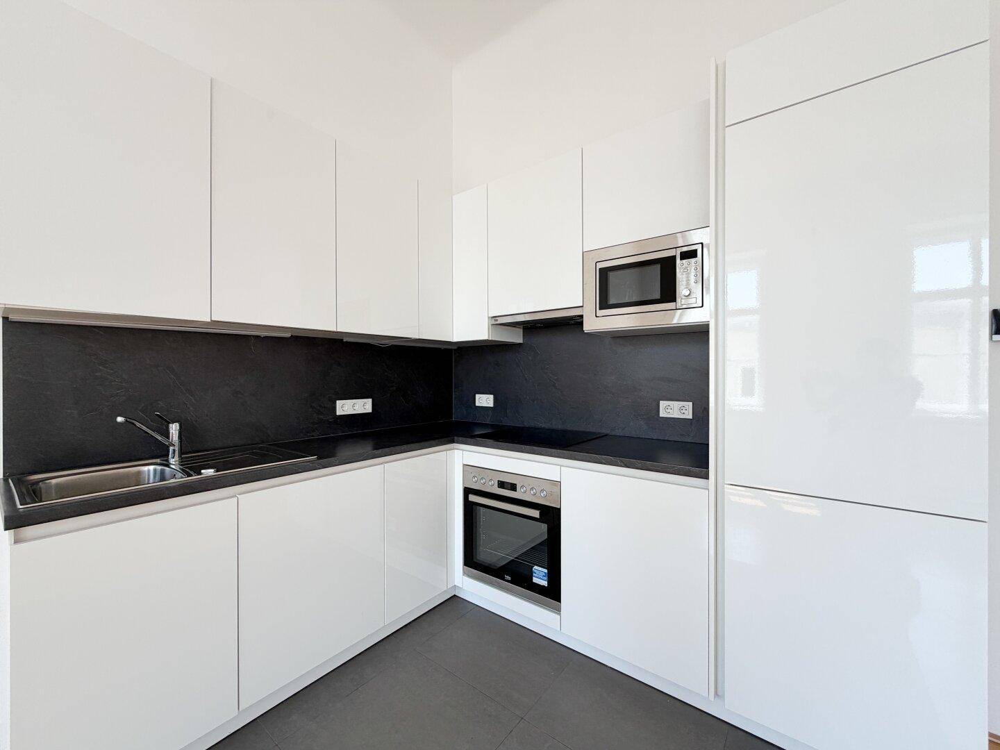Moderne weiße Einbauküche mit glänzenden Fronten, integriertem Backofen und Mikrowelle.