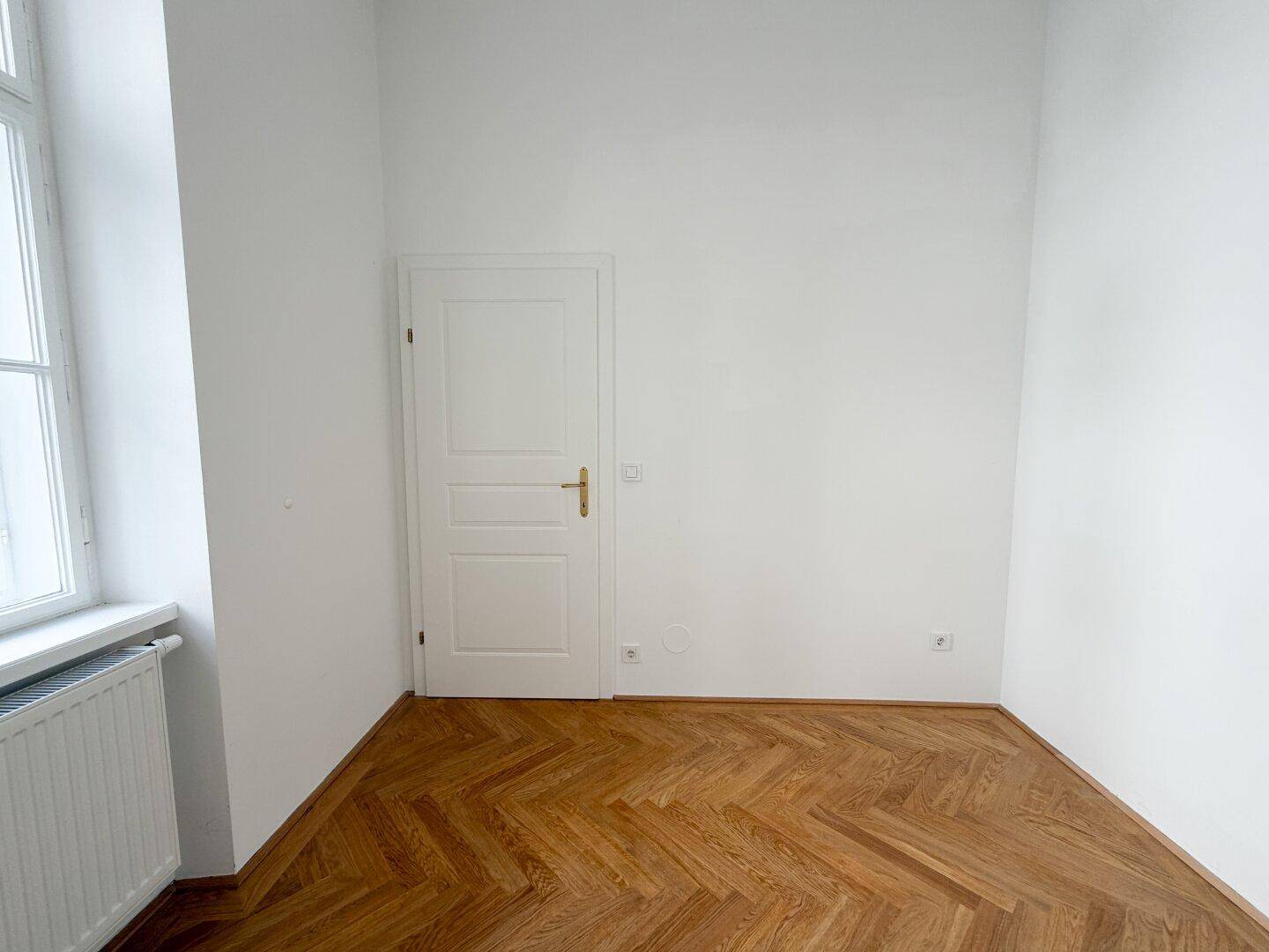 Leeres Zimmer mit klassischem Fischgrätparkett und weißer Tür, bereit zur individuellen Gestaltung.